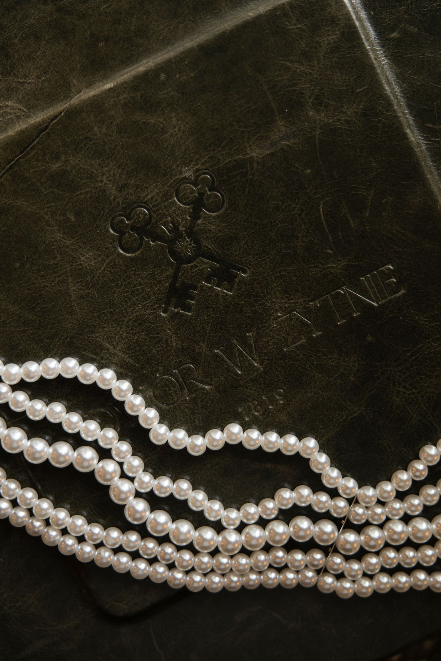 Elegant pearl necklace strands draped over a dark green leather book with embossed key design.