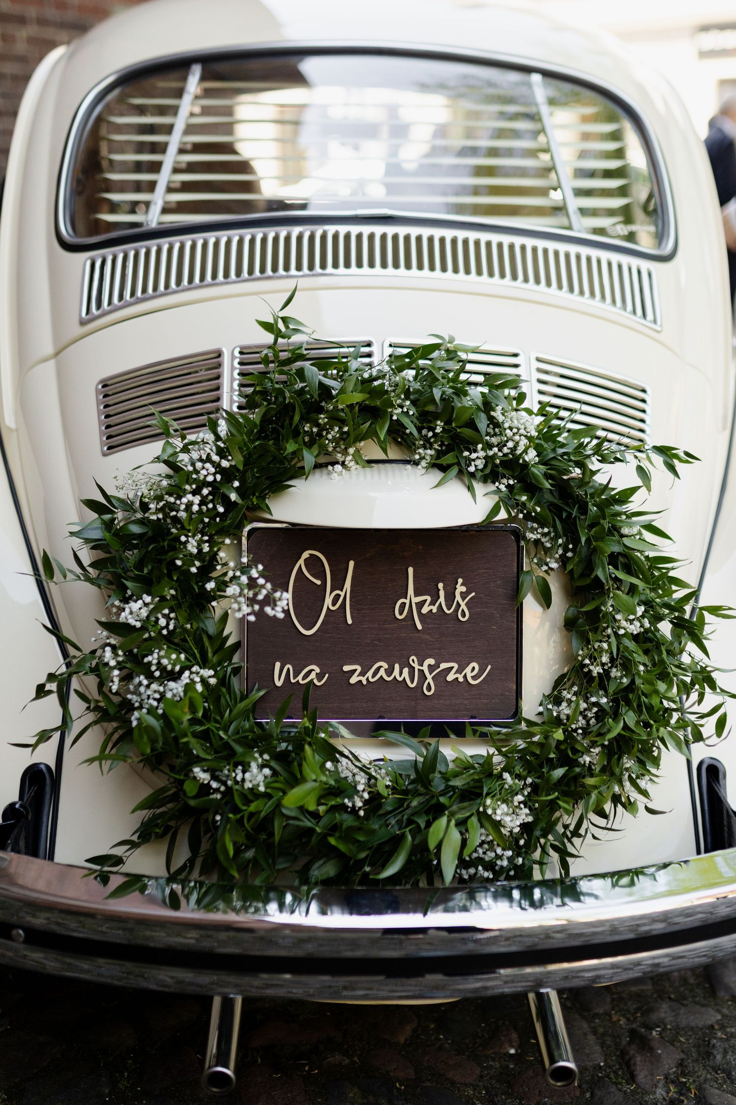 Vintage white Volkswagen Beetle decorated with a lush green wedding wreath and sign on the back window.