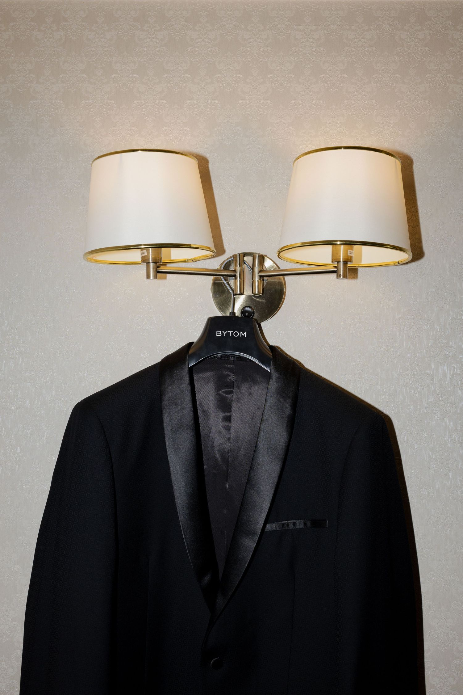 A black tuxedo jacket hangs beneath two wall-mounted sconce lights with white lampshades.
