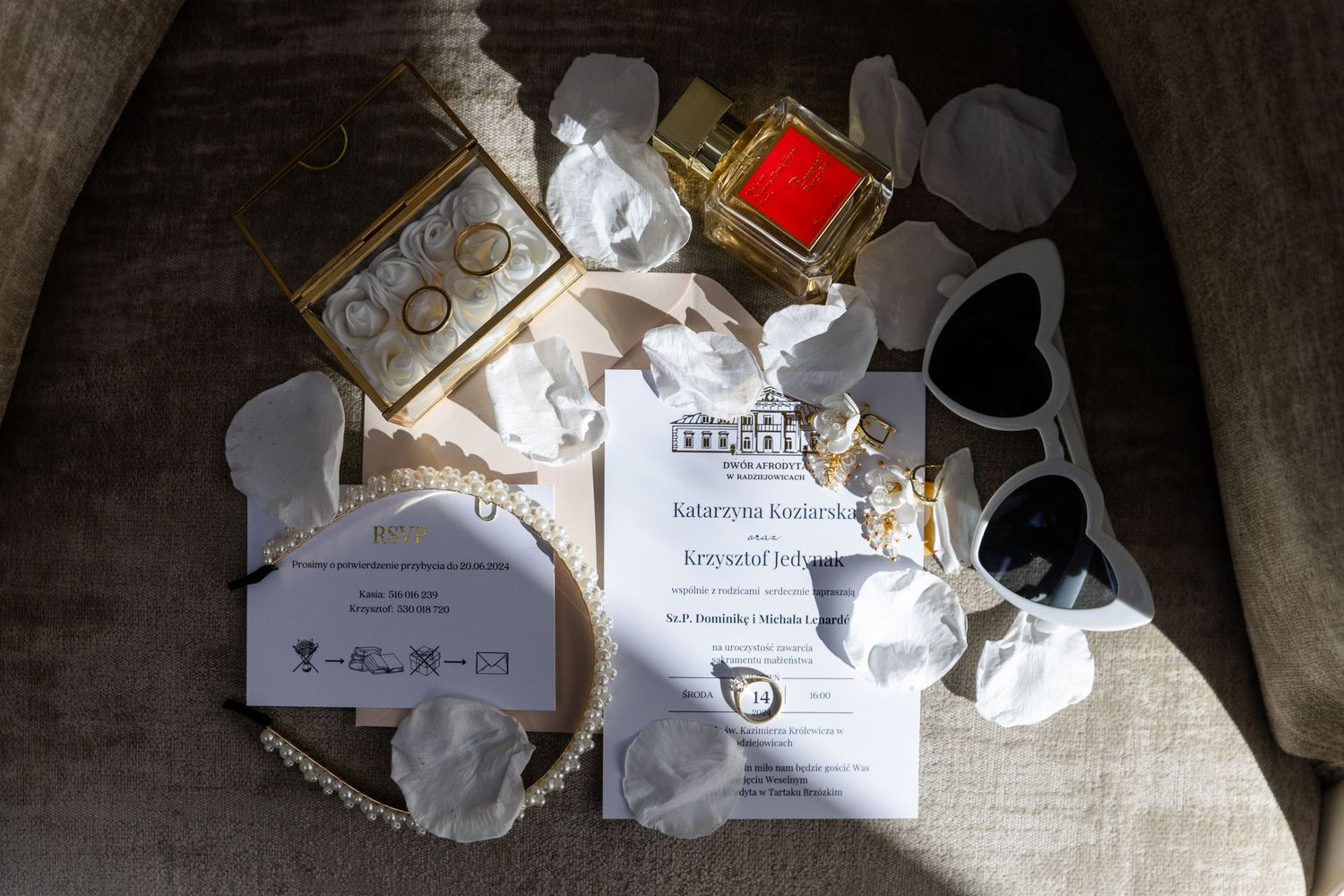 Scattered wedding invitation cards and envelopes with white ribbons and ornate details on a textured fabric background.