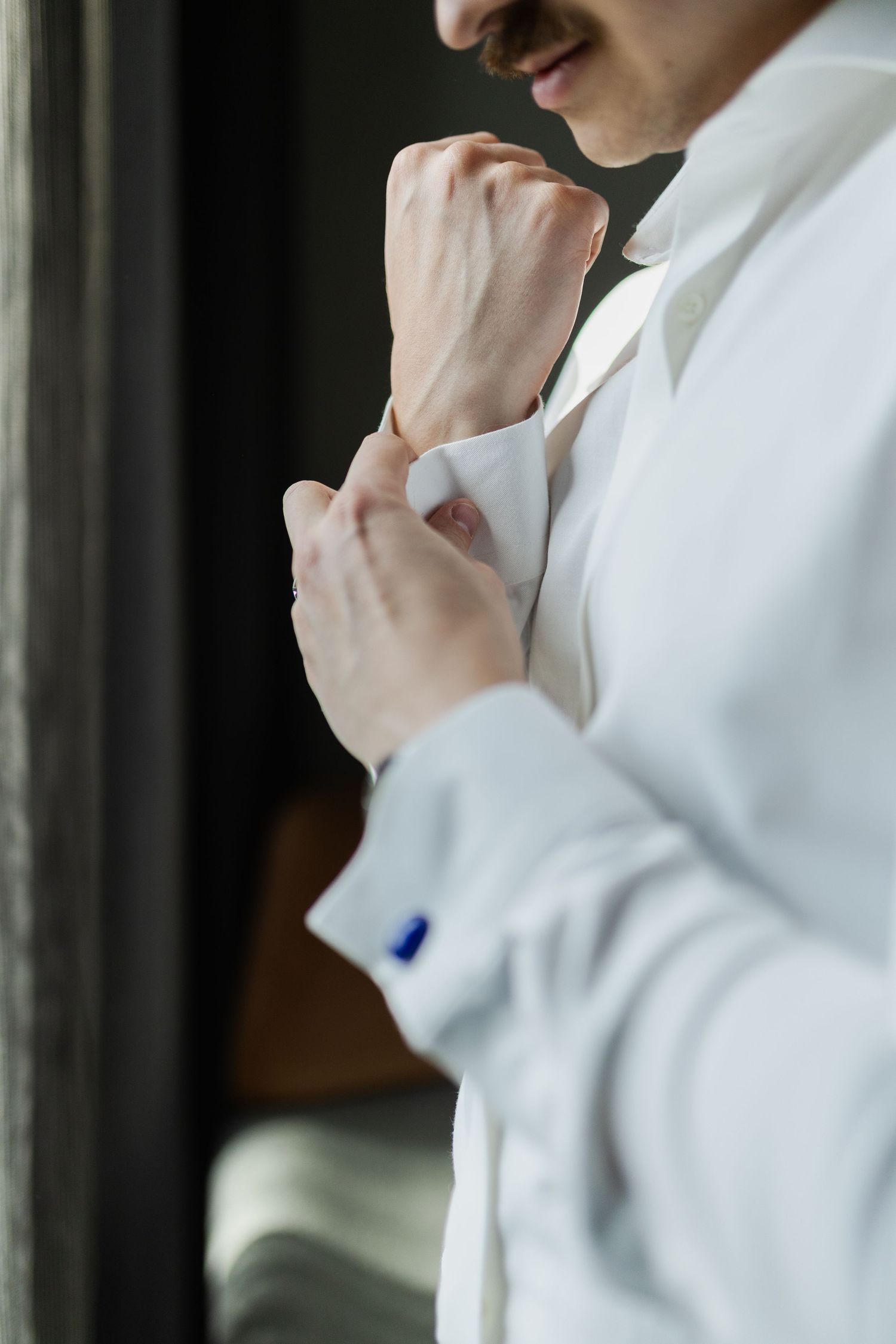 Close-up of hands adjusting cufflinks on a crisp white dress shirt with blue button detail.