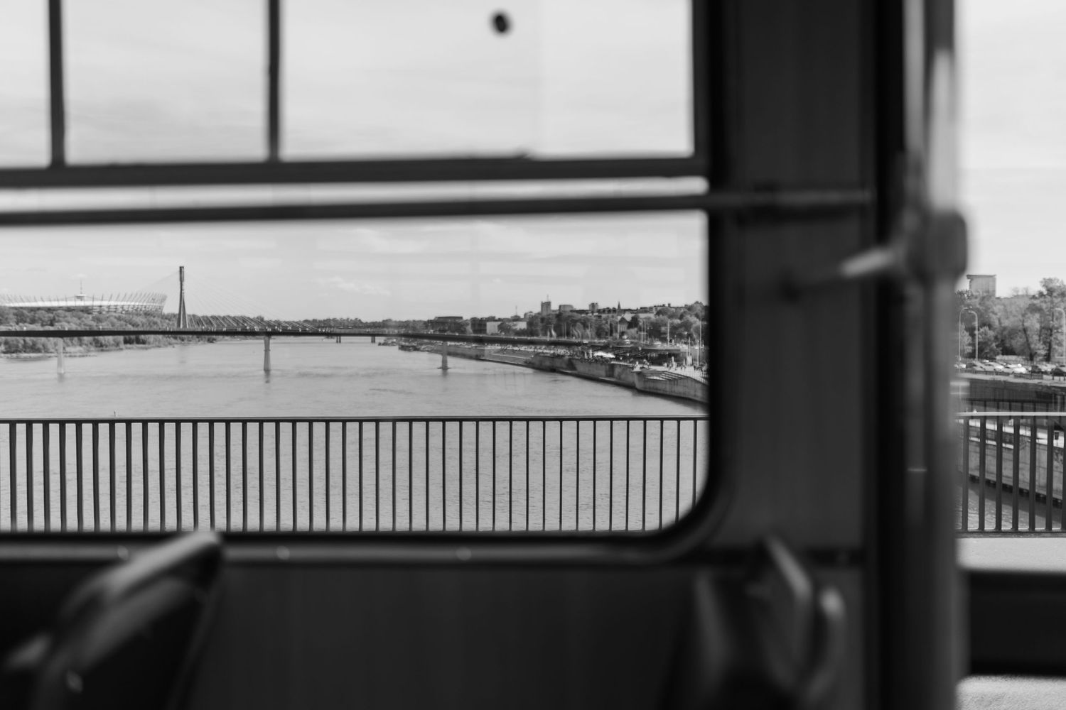 Black and white view of a river and cityscape seen through a window or railing on a bridge.