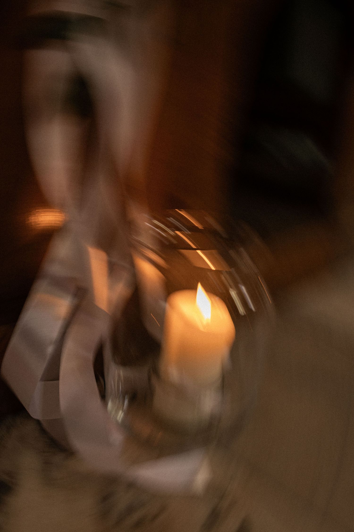 A blurred artistic photograph of a glowing candle flame casting warm light through glass in a dark moody setting.