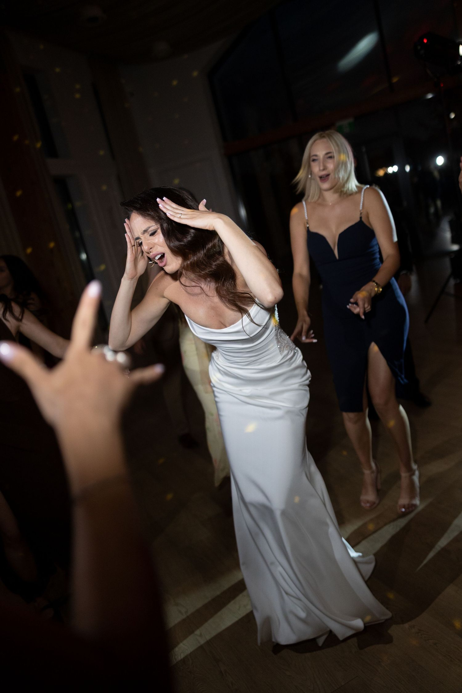 Women dancing elegantly at a formal event, one in a white satin gown laughing joyfully while another in navy dress looks on.