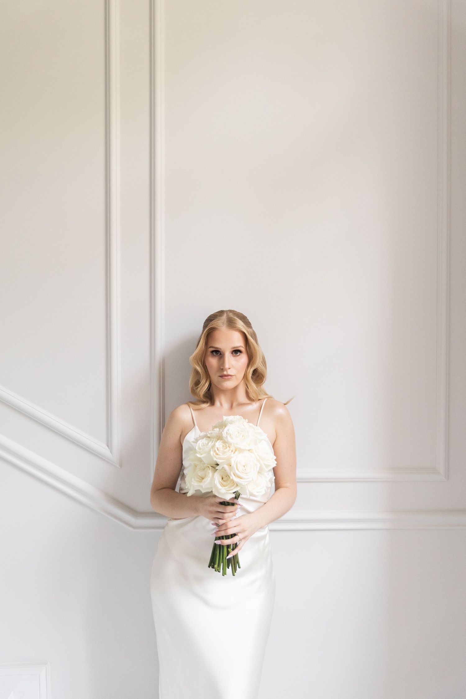 A minimalist bridal portrait series against white walls showcasing an elegant white wedding dress and bouquet.