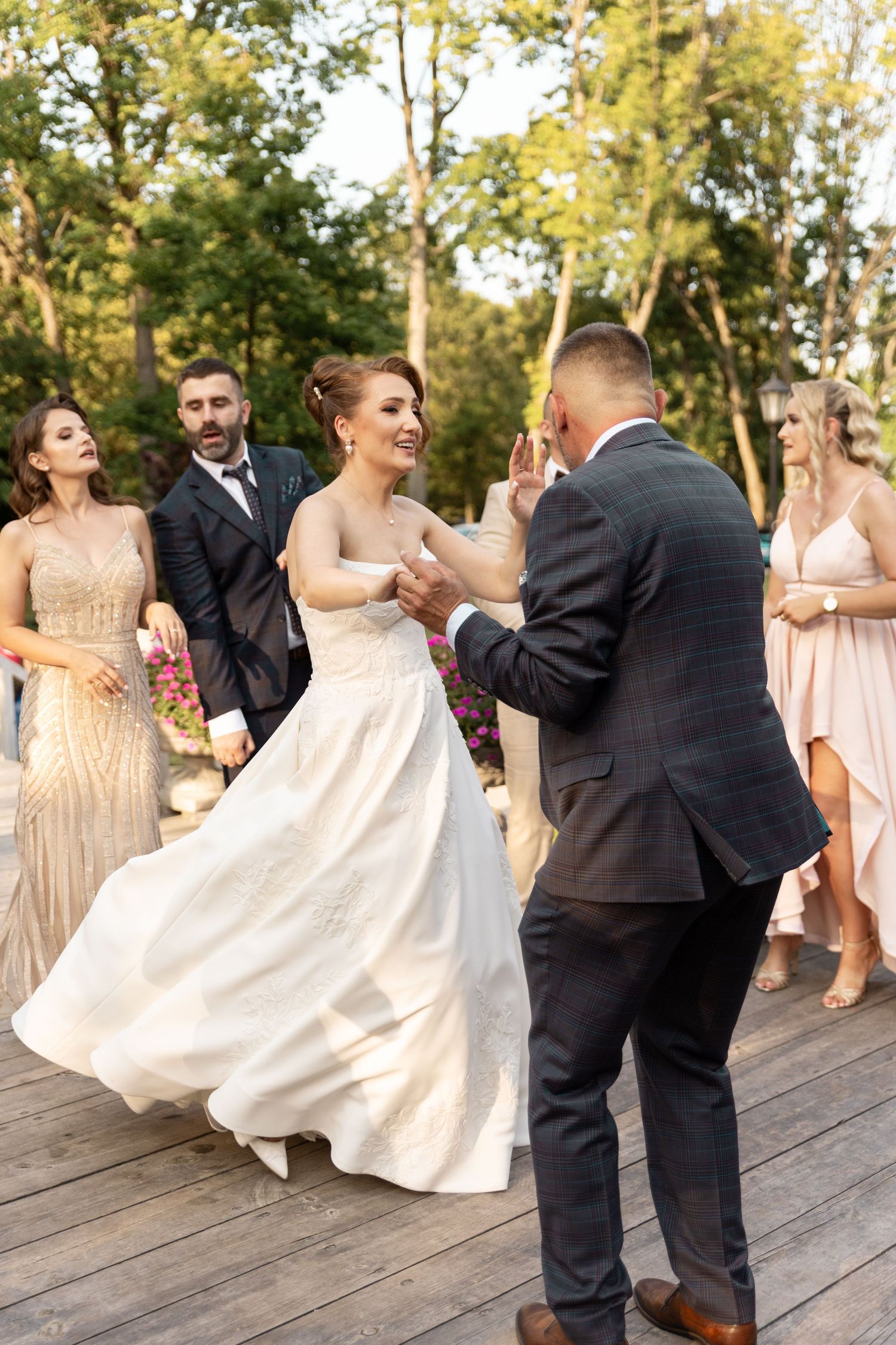 Wedding party members dance joyfully on a wooden deck during golden hour celebrations.