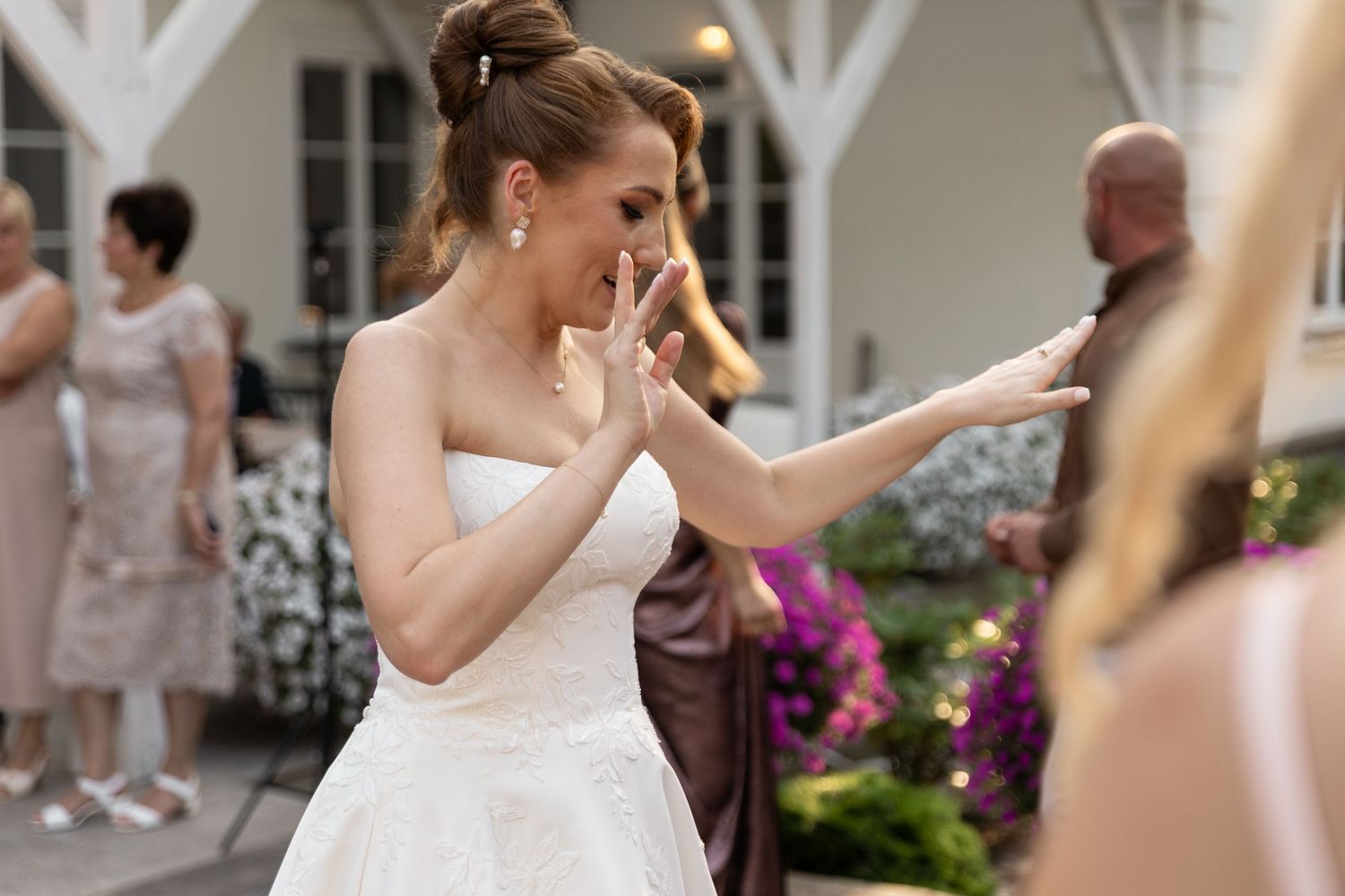 A bride in a white wedding dress dances with guests at an outdoor reception area.