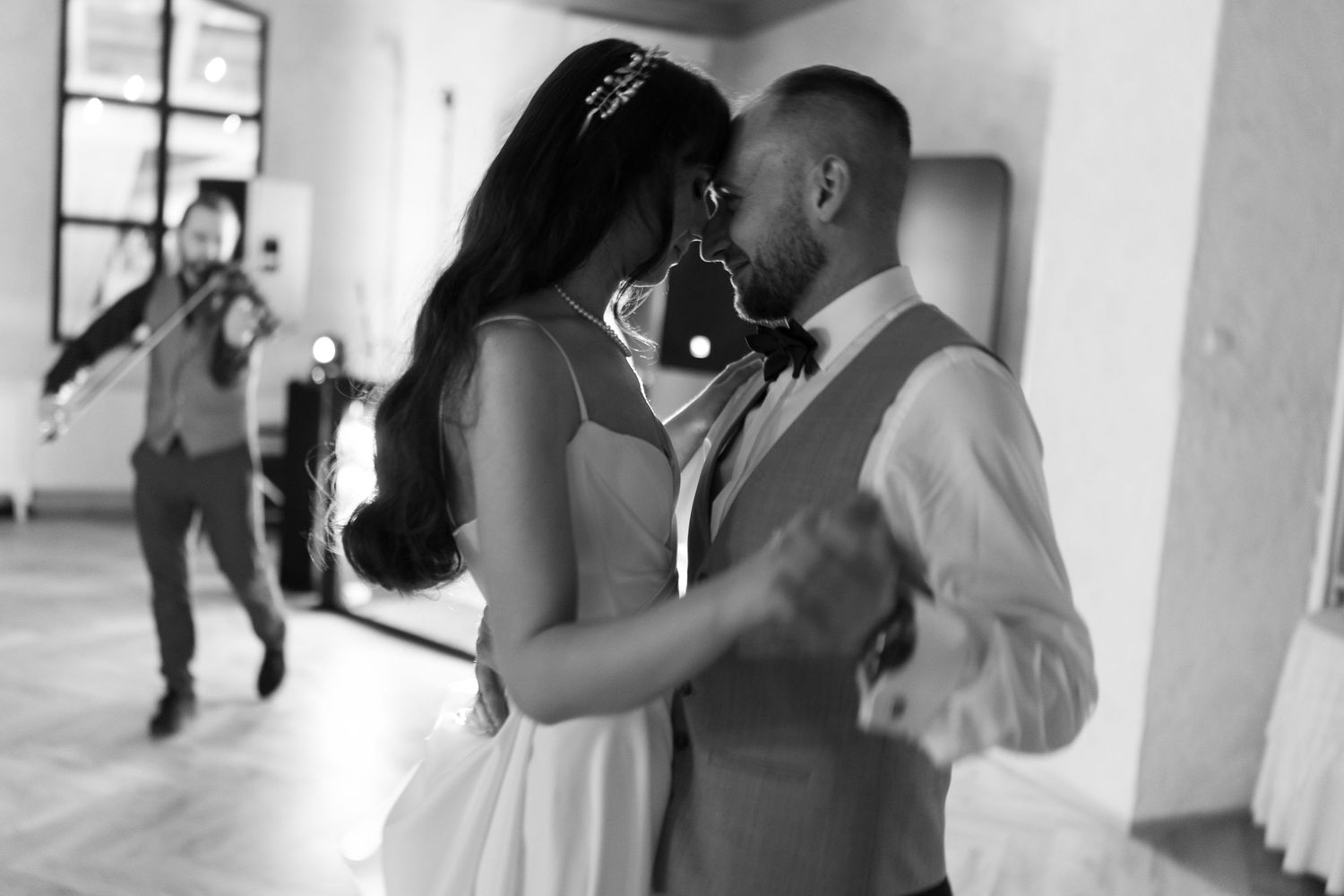 A black and white photograph captures an intimate dance moment between a couple at their wedding reception.