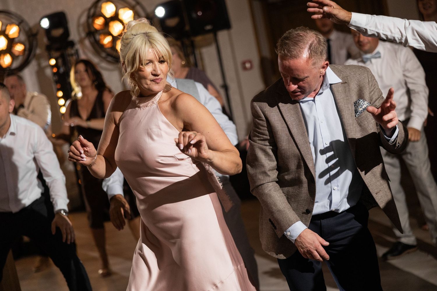 Guests dancing energetically at a wedding reception in an elegant venue with warm stage lighting.