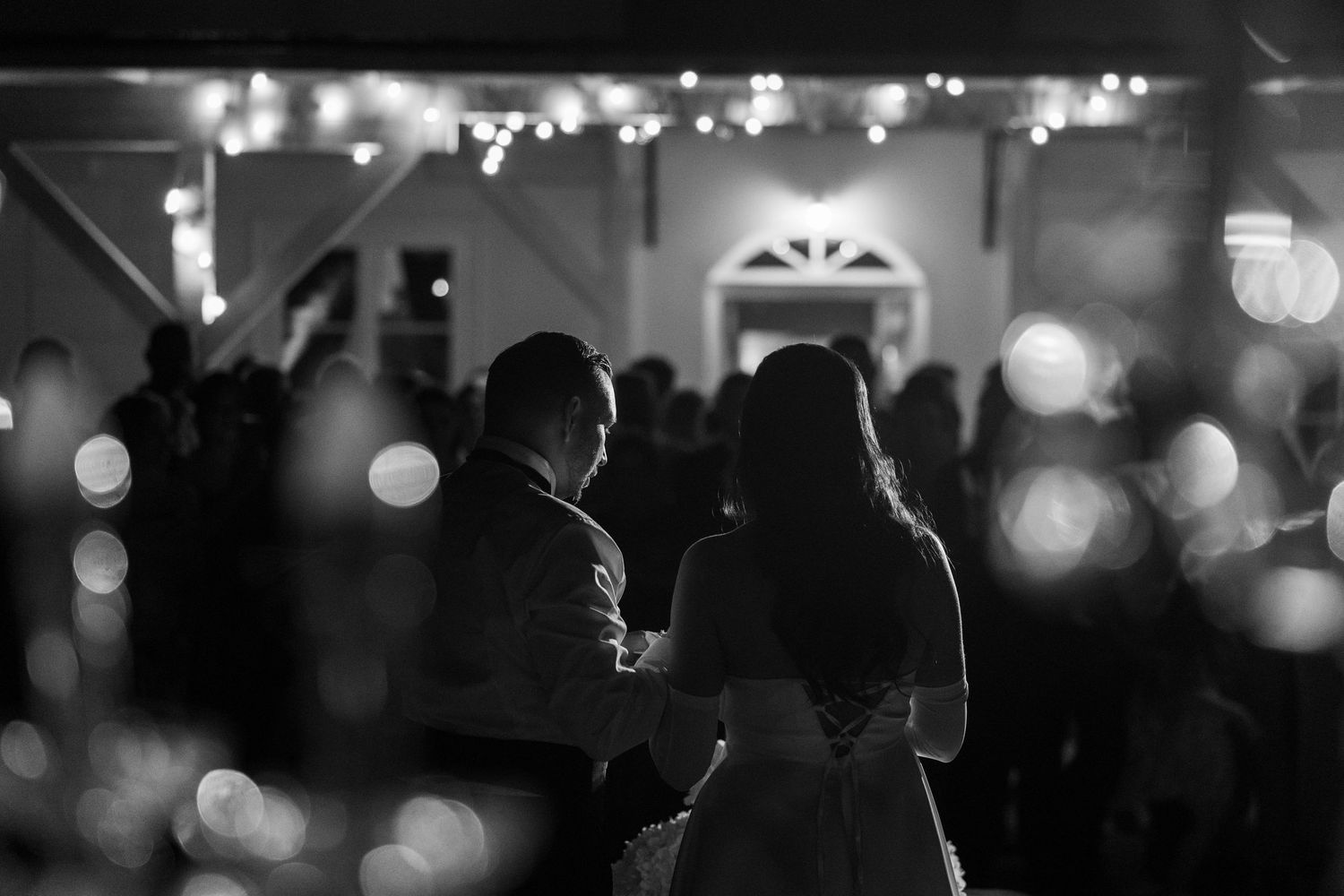 Black and white photo of a couple sharing their first dance at a romantic wedding reception with bokeh lights.