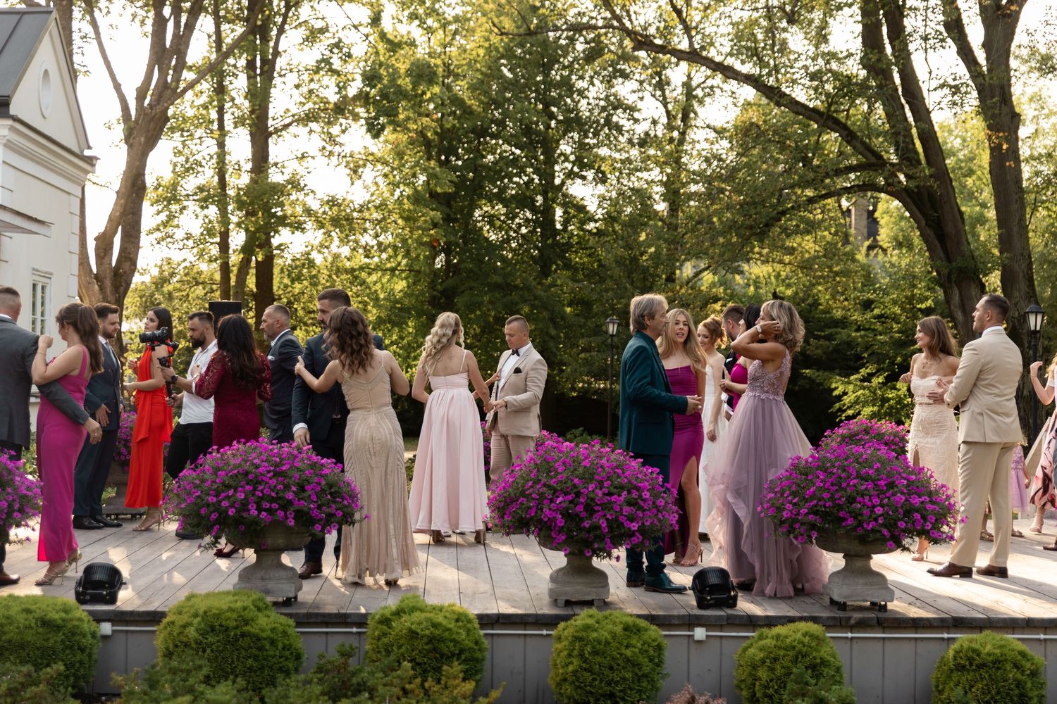 Wedding party members stand together on a patio surrounded by vibrant purple flowers during an outdoor ceremony.