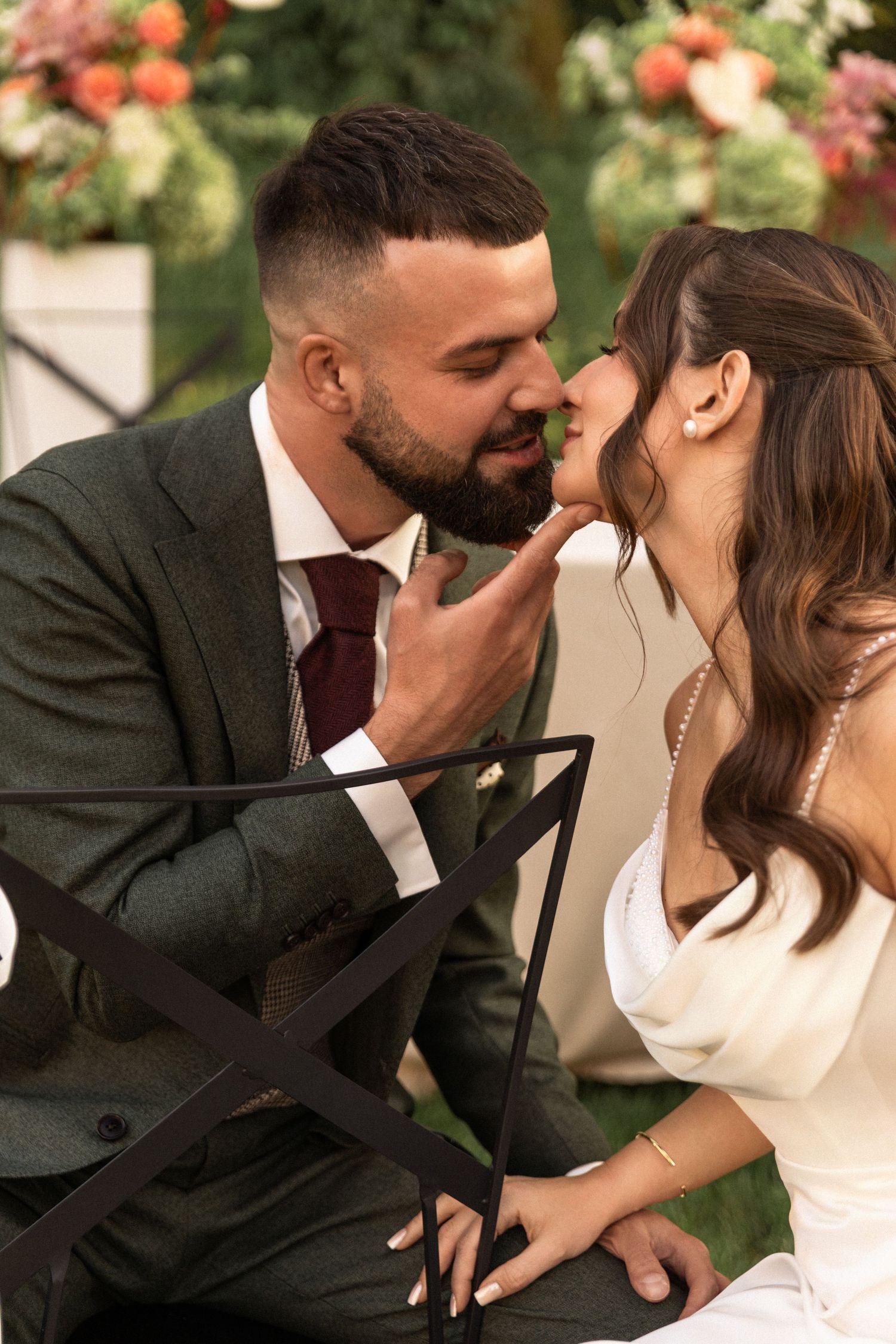 Romantic wedding couple share an intimate moment in a garden setting with coral flowers in the background.