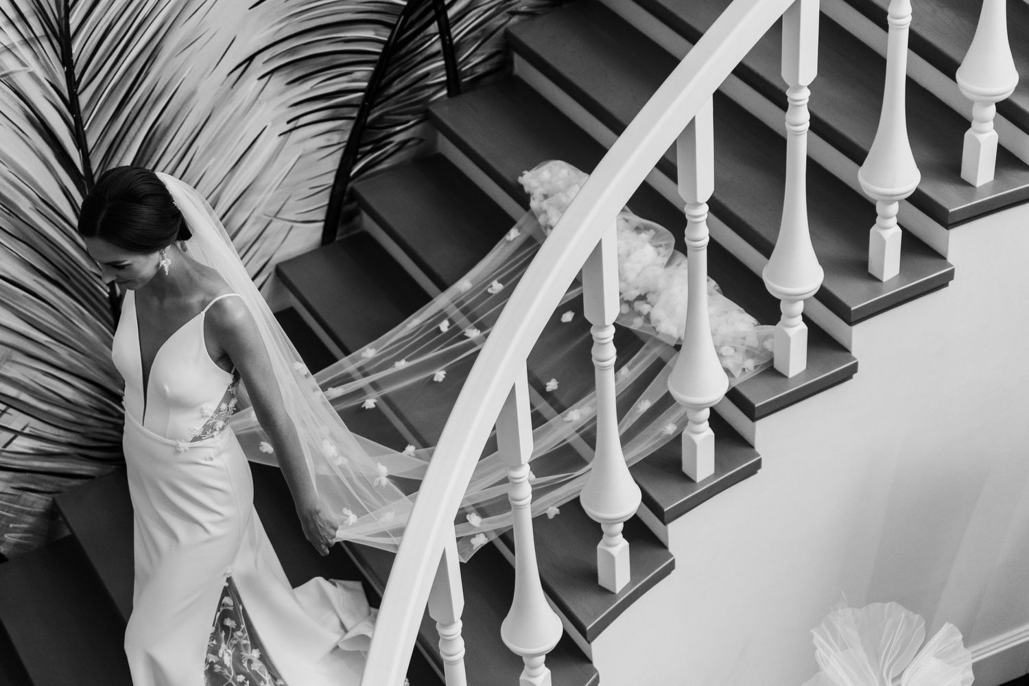 A candid black and white wedding scene captured on a staircase with white banisters and a palm frond in view.