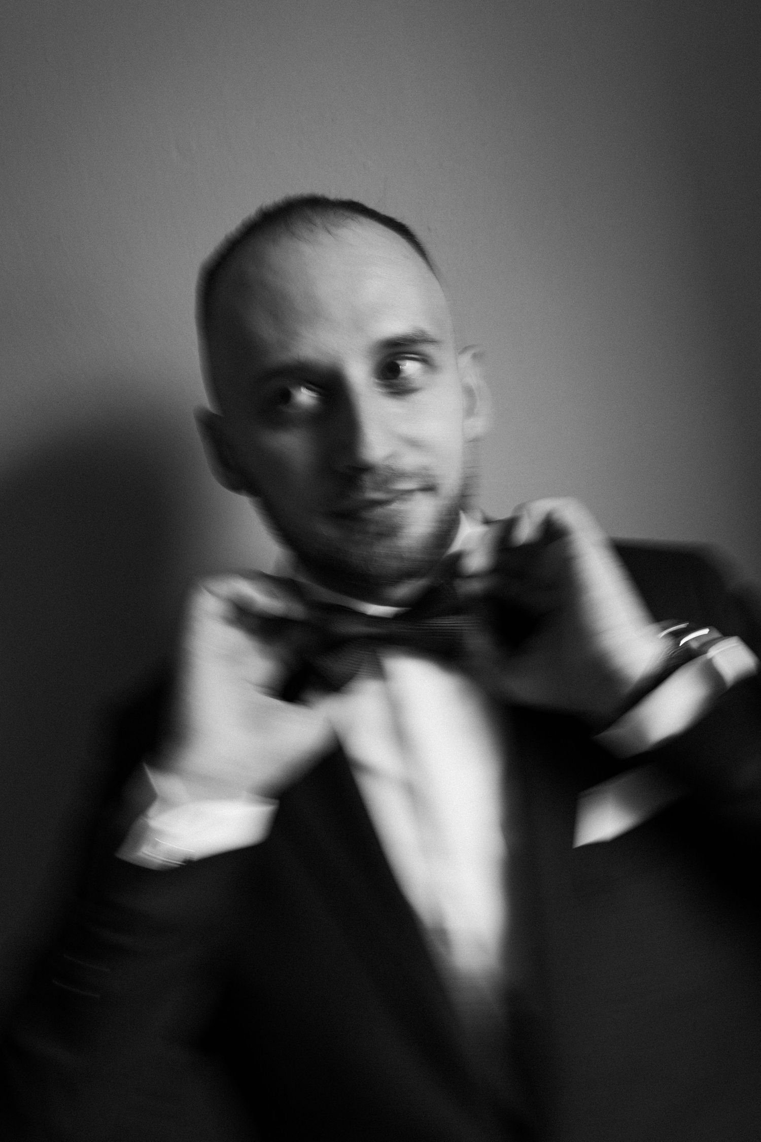 Black and white portrait in a tuxedo and bow tie with a playful sideways glance and smirk.