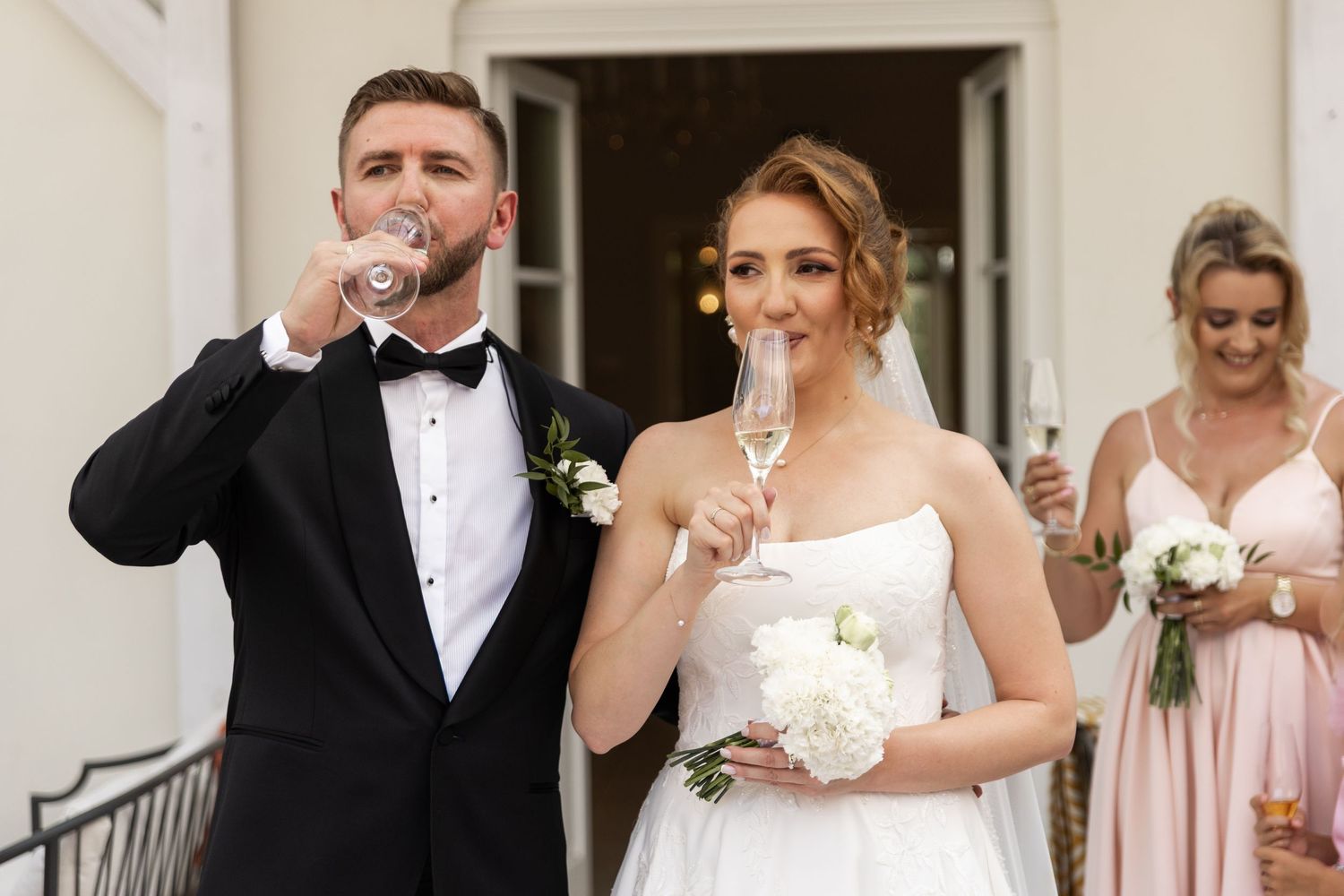 Wedding party in formal attire holding champagne glasses for a celebratory toast on outdoor steps.