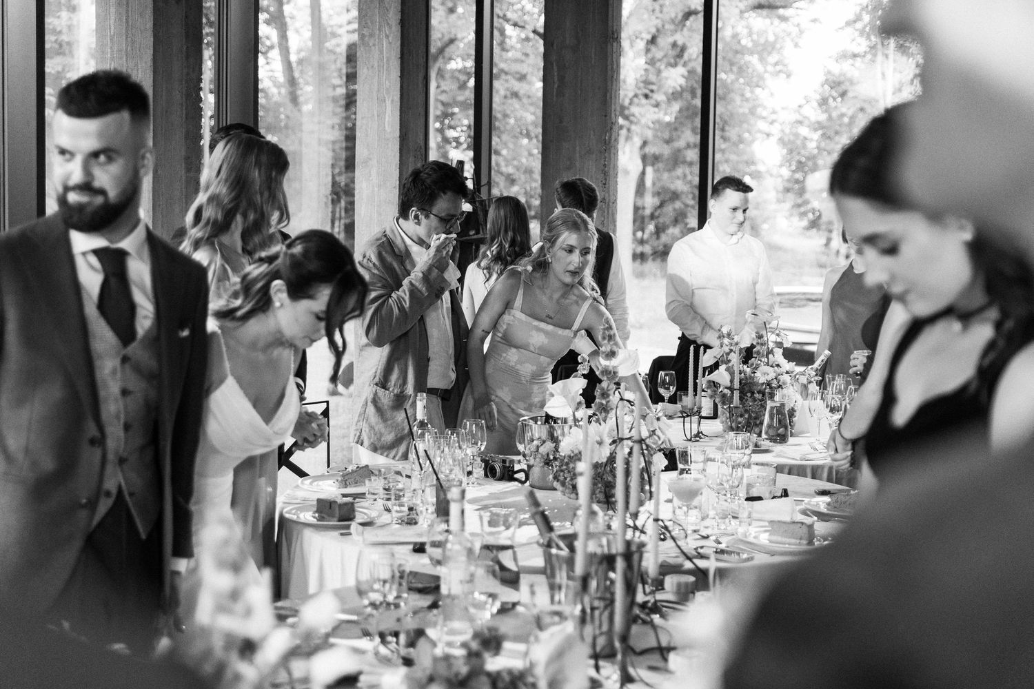 Black and white photo of wedding reception guests seated at an elegant long dining table with place settings and centerpieces.