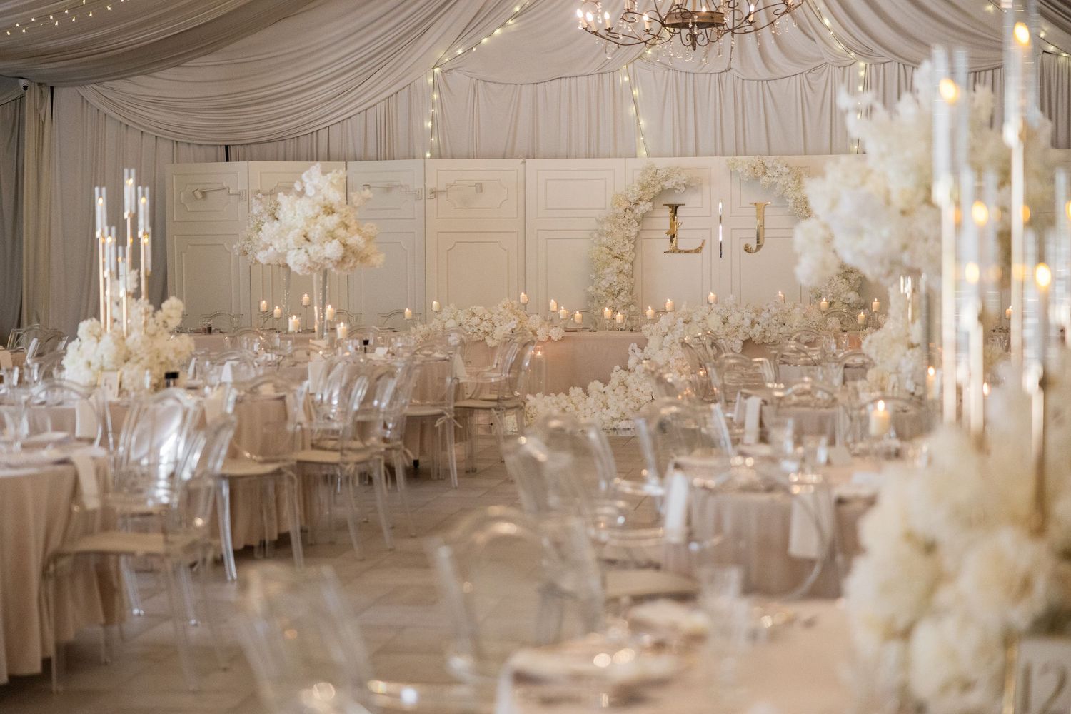 Elegant all-white wedding reception with floral centerpieces, crystal candelabras, and draped ceiling in a luxurious ballroom.