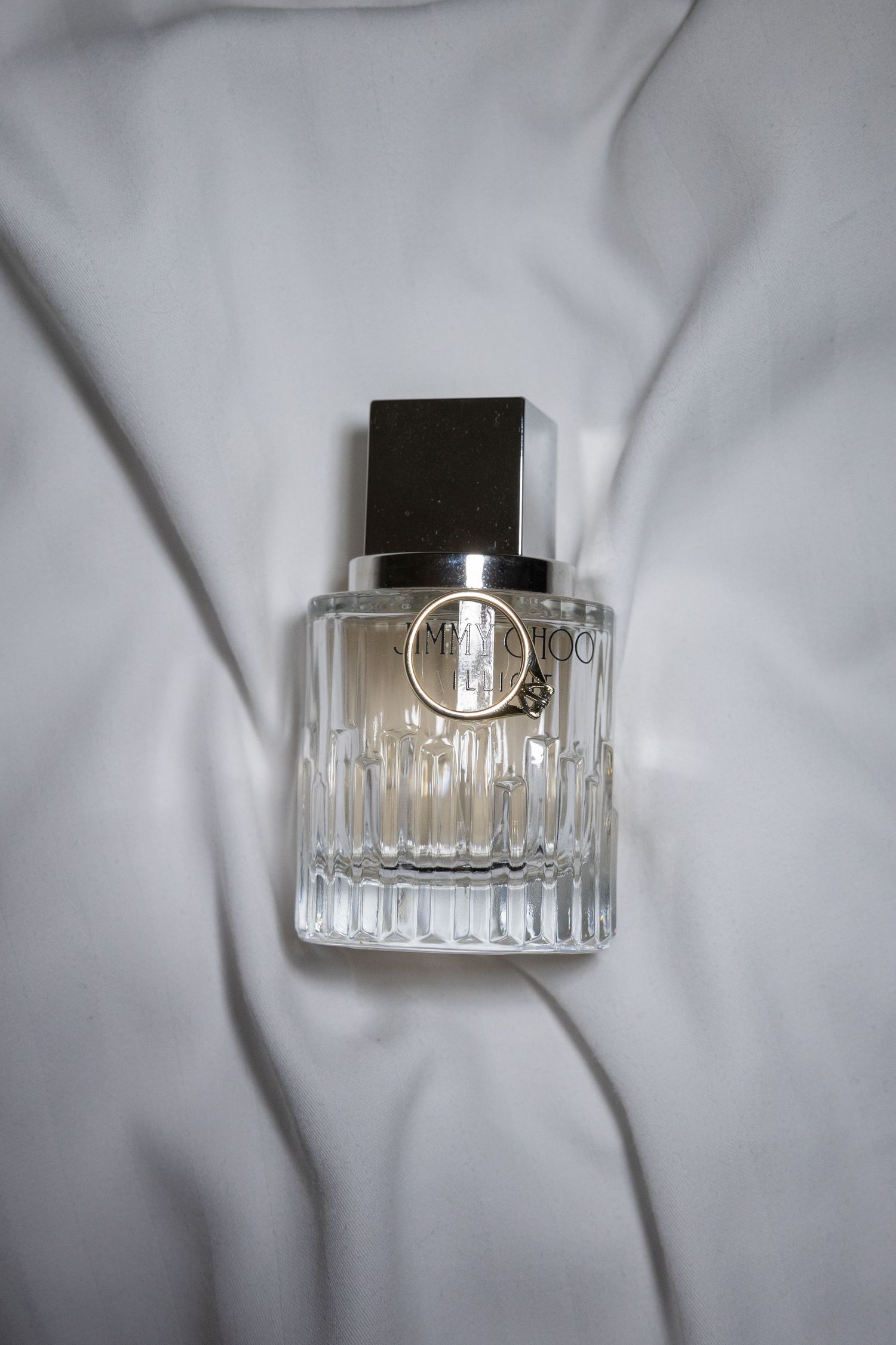 Jimmy Choo perfume bottle with crystal-cut glass and dark cap displayed on white silk fabric.