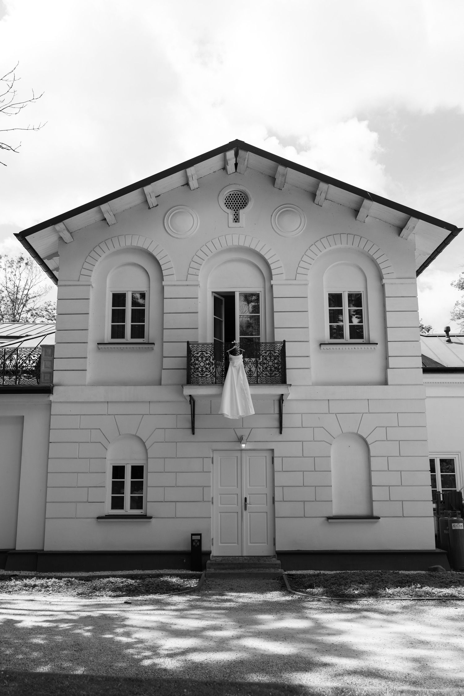 Black and white photo of a elegant two-story building with arched windows and a wedding dress hanging from the balcony.