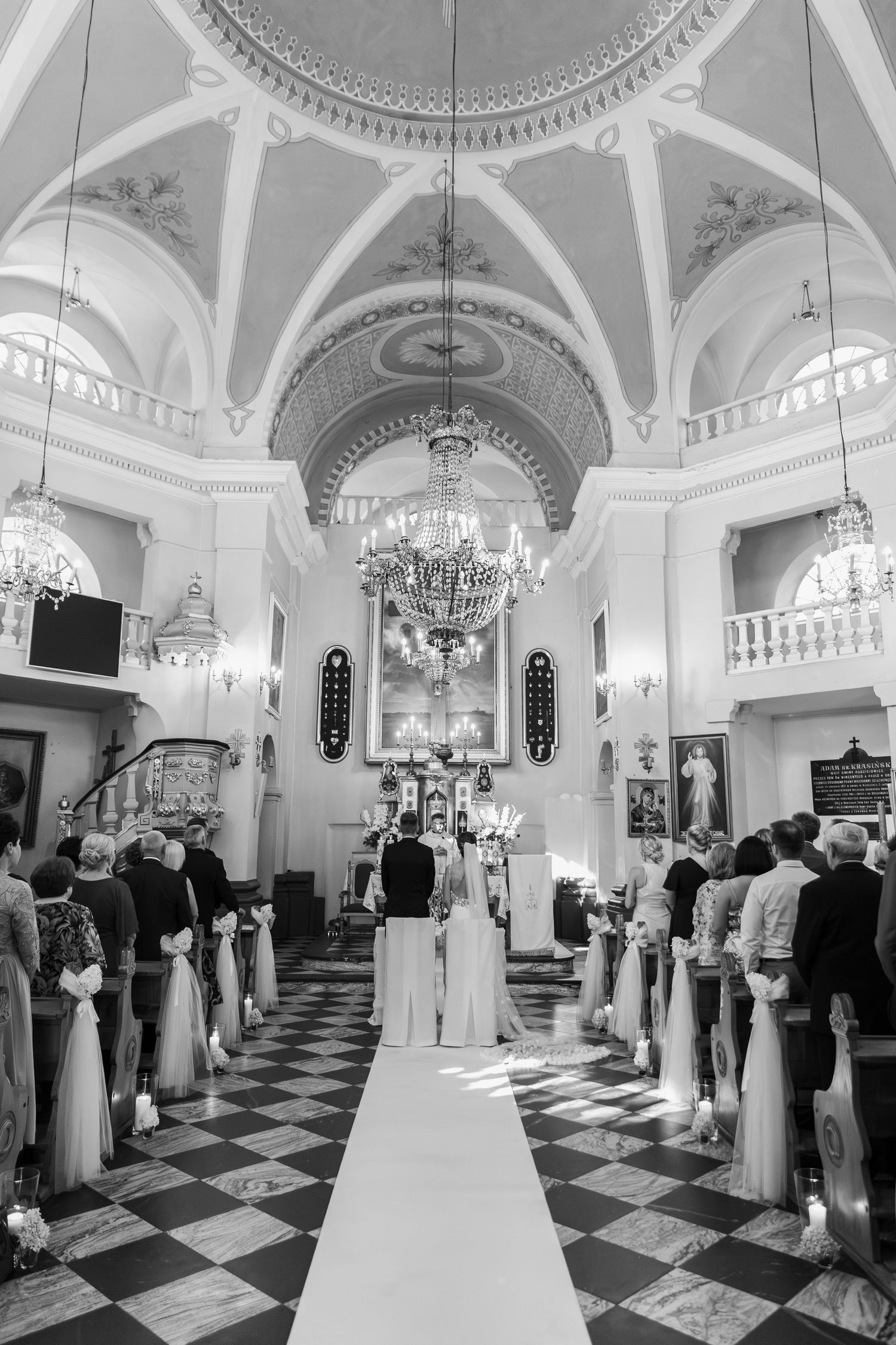 Black and white photo of a traditional church wedding ceremony with guests seated in pews under ornate vaulted ceilings.