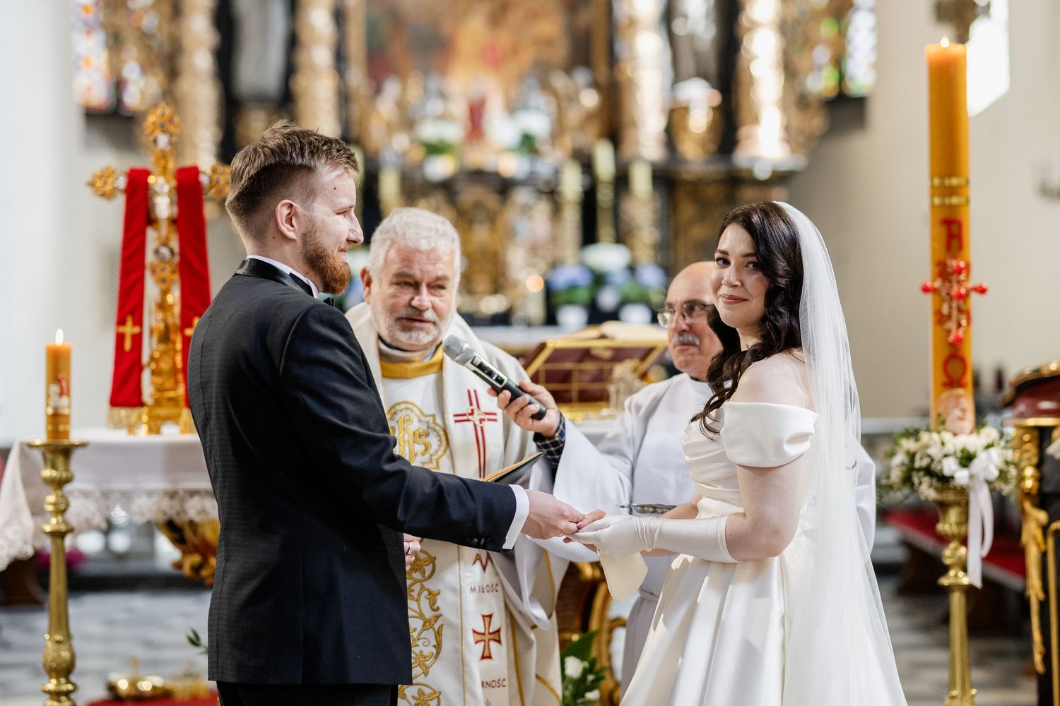 A couple exchanges vows during their wedding ceremony at a church altar with lit candles and ornate decorations.