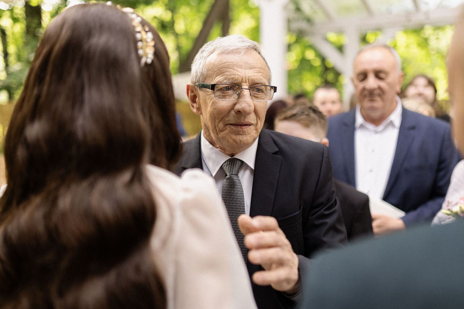 An emotional moment captured during an outdoor wedding ceremony as people interact under natural sunlight.