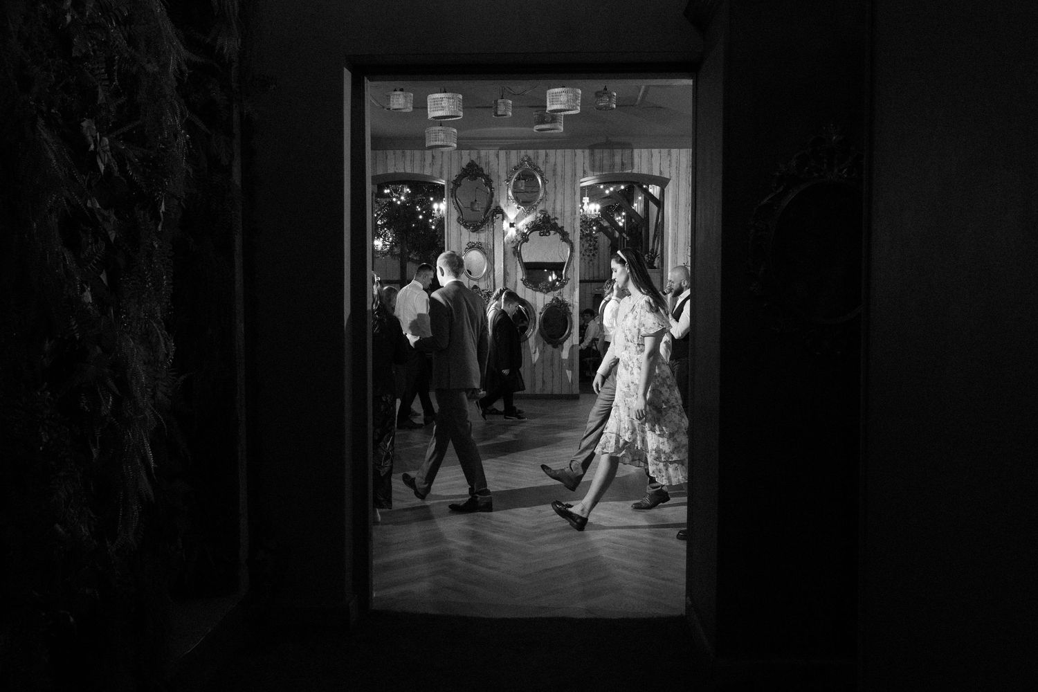 Black and white photograph showing people dancing in a social setting viewed through a doorway.