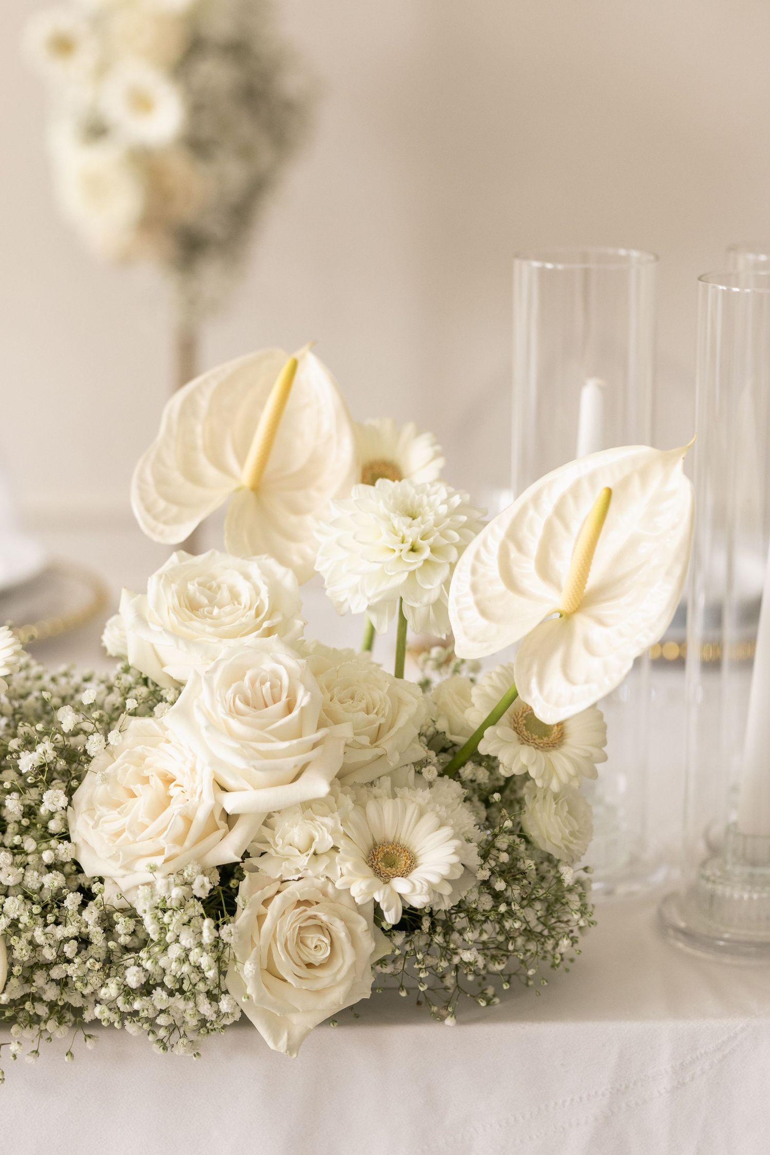 Elegant white roses and baby's breath floral arrangement with glass vases on a light neutral surface.