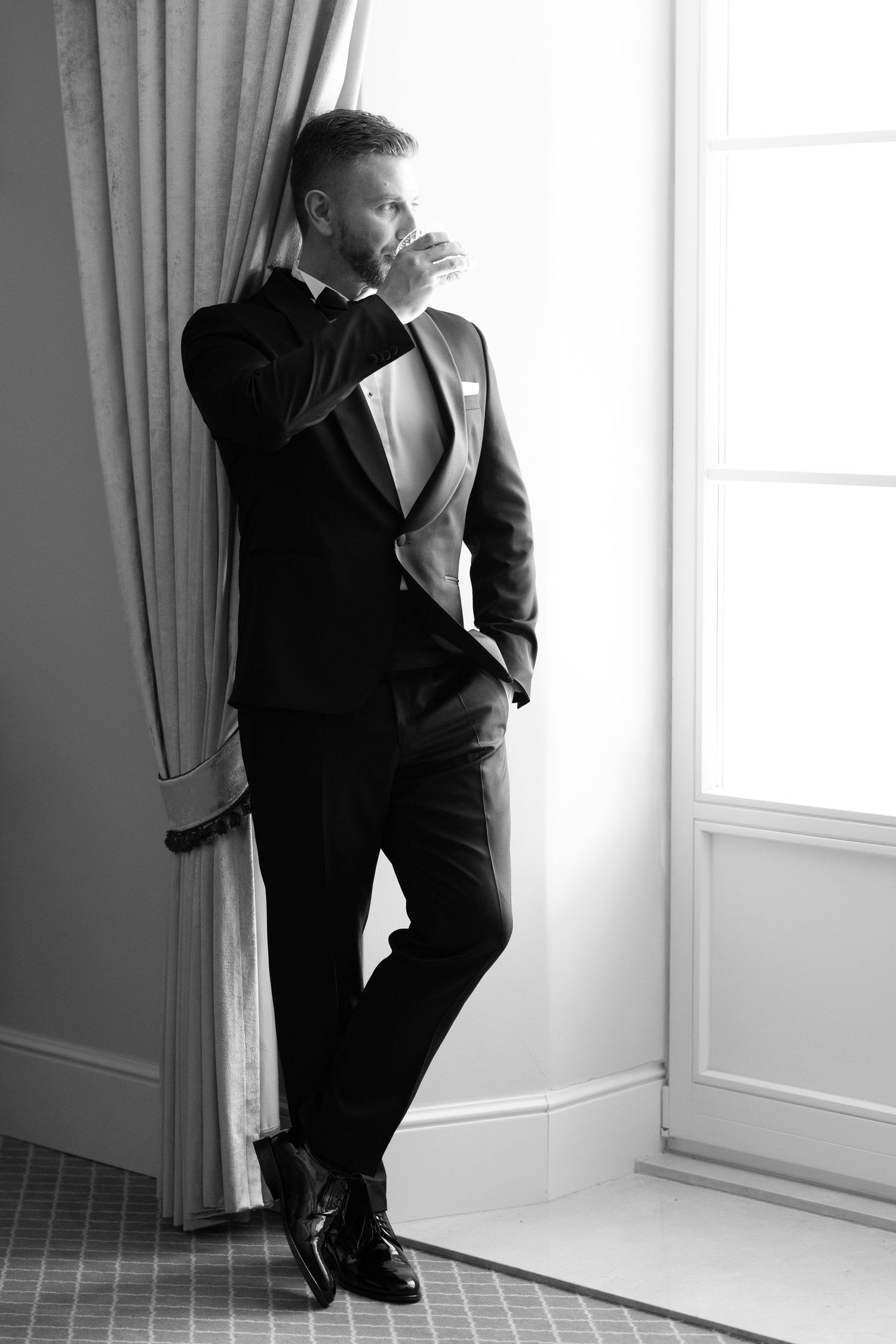 Black and white photo series showing a person in a dark suit leaning against a bright window and wall in an empty room.