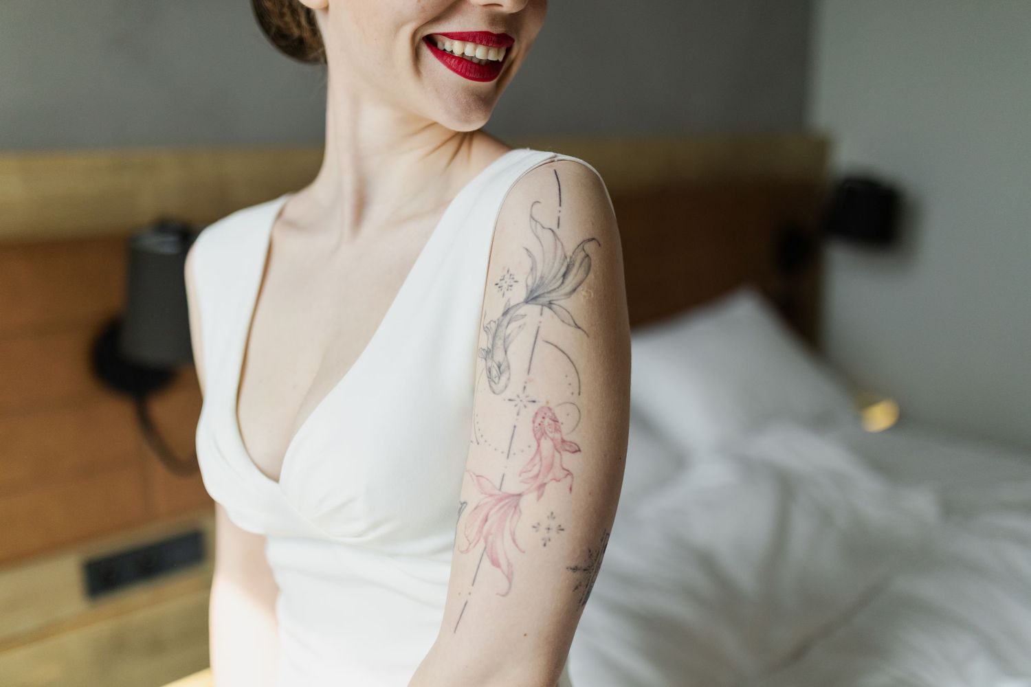 A delicate floral tattoo outlines shown on an arm wearing a white v-neck dress against a light interior background.