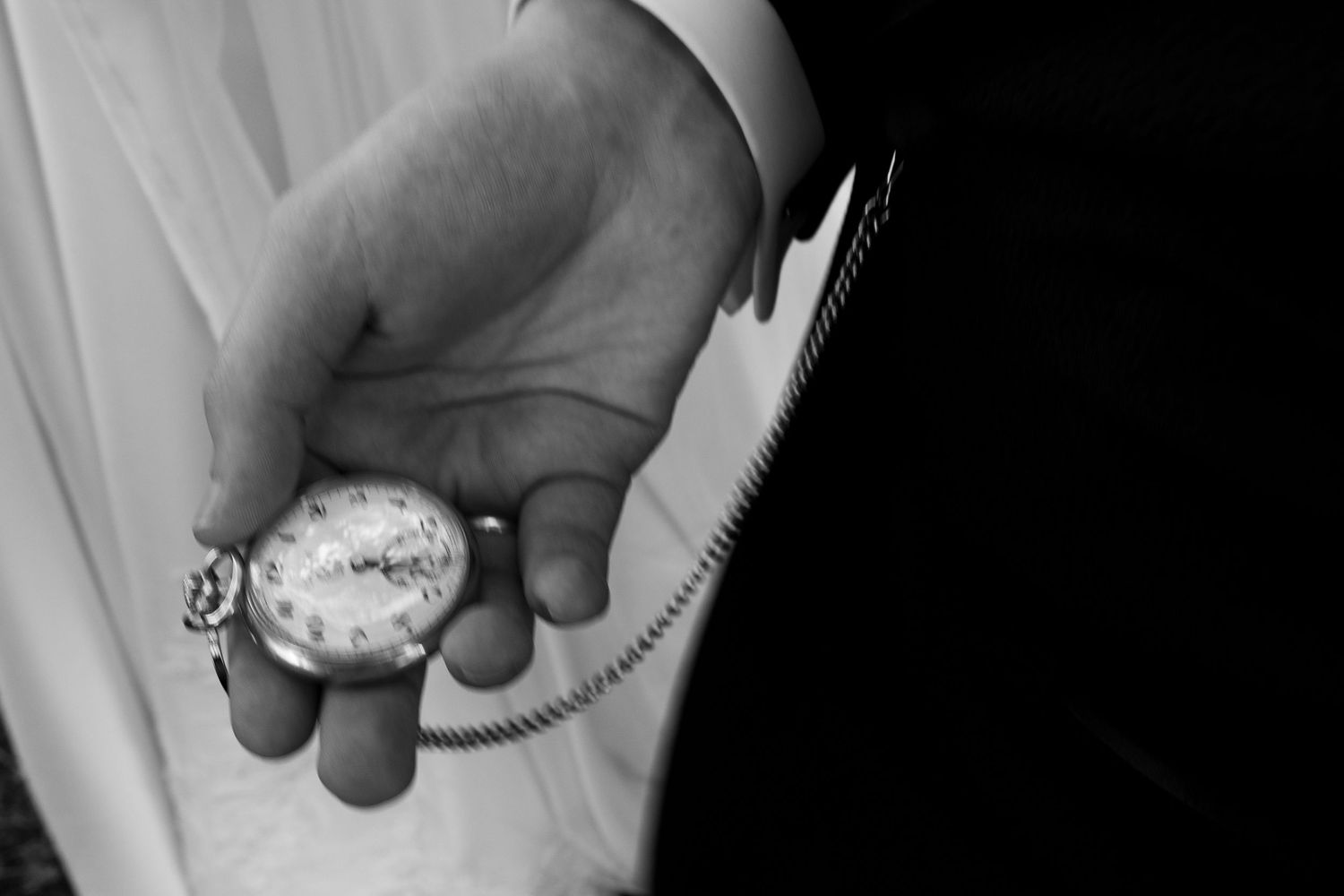 Black and white close-up image of a hand holding a vintage pocket watch against a dark background.