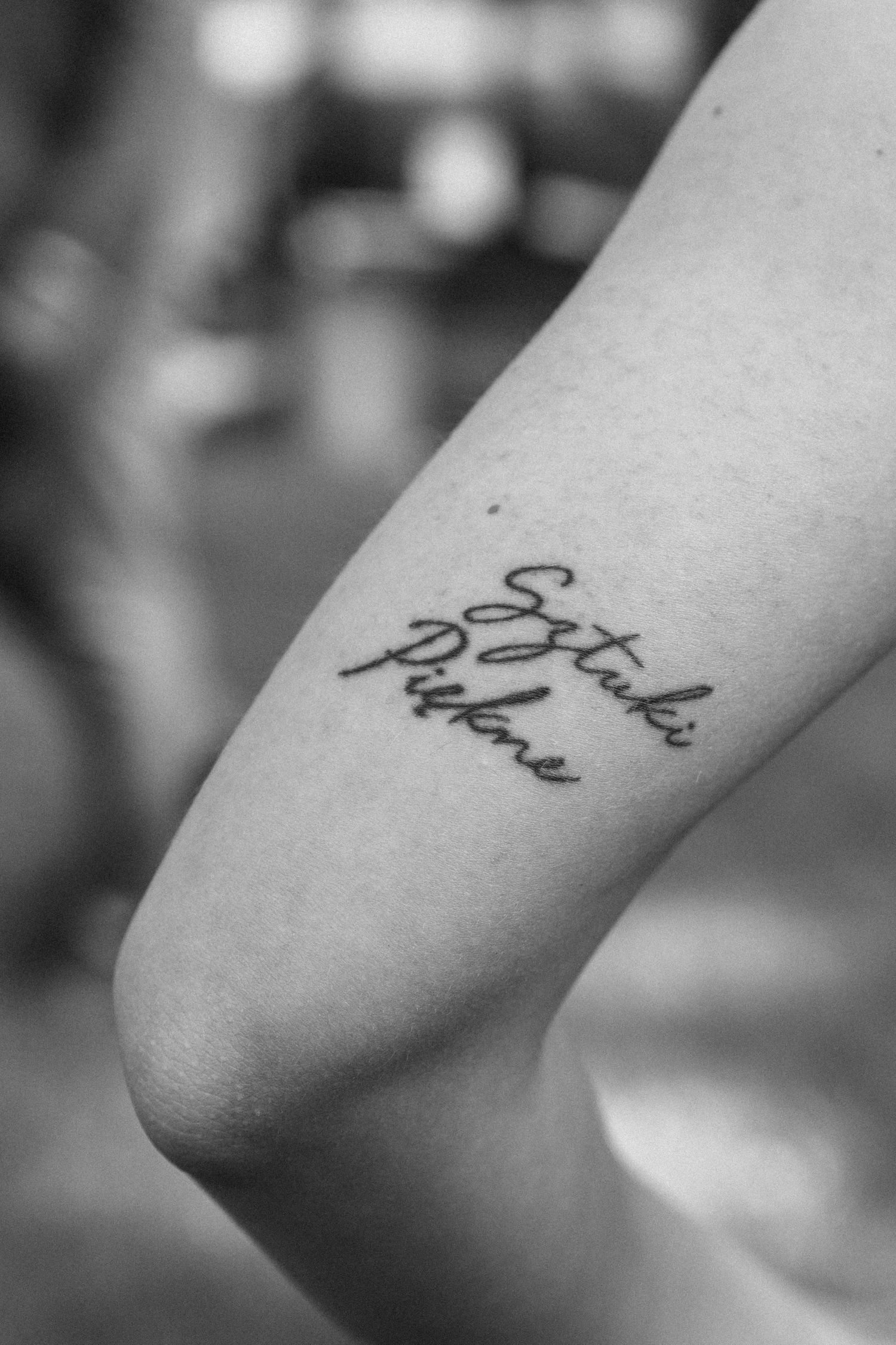 A delicate script tattoo in black ink placed on an arm, shown in black and white photography.