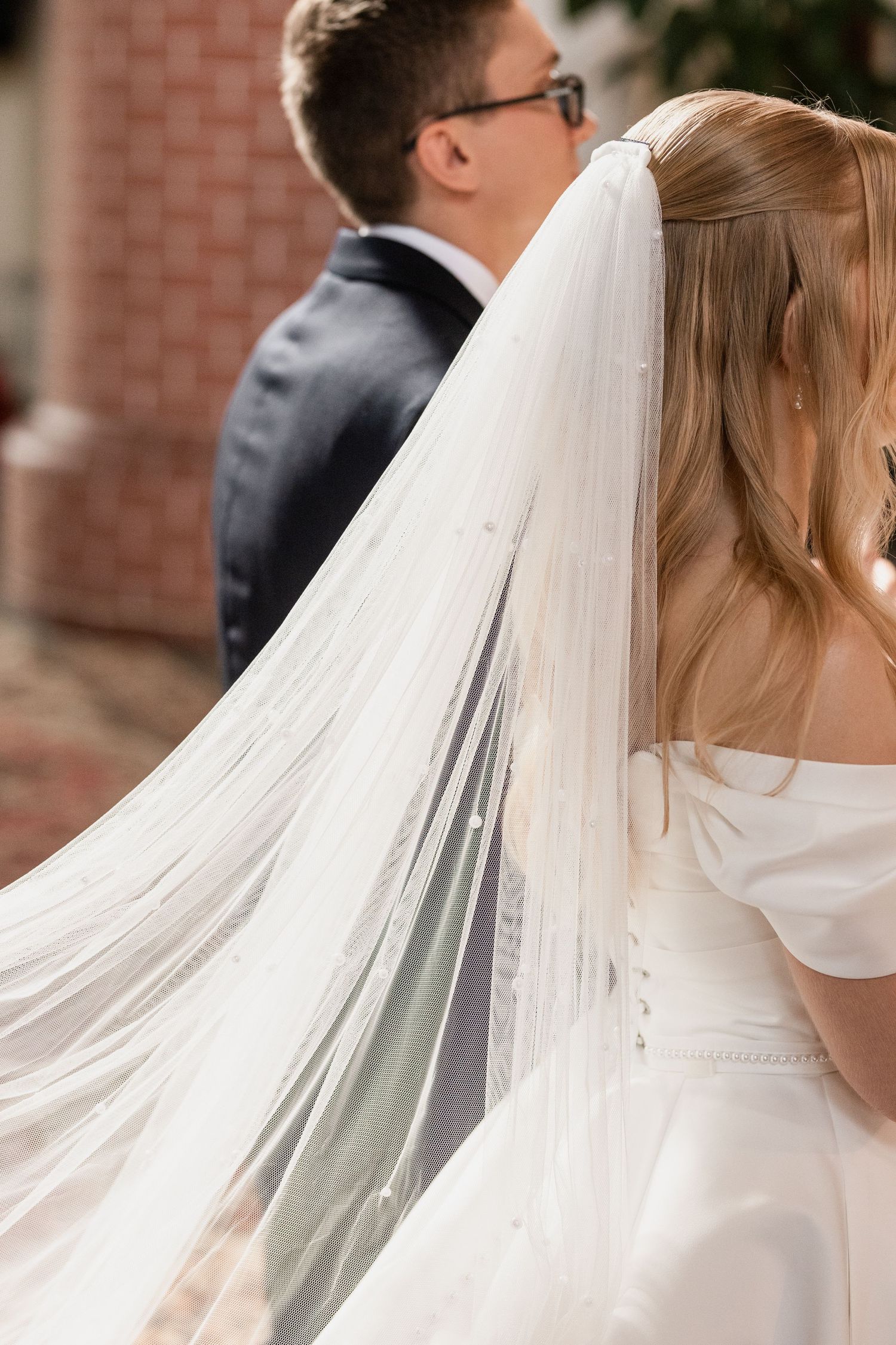 A close-up view of a bride's flowing white veil and wedding dress as she stands next to her groom in a dark suit.