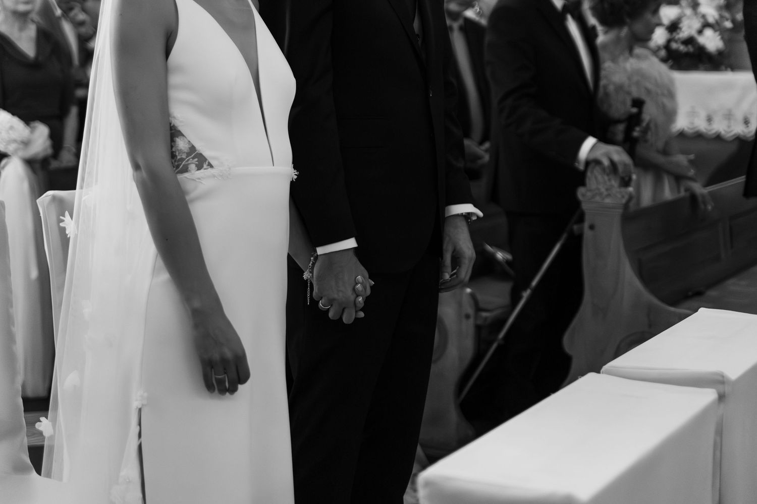 Black and white image showing a couple holding hands at a wedding ceremony with a sleek modern white gown.