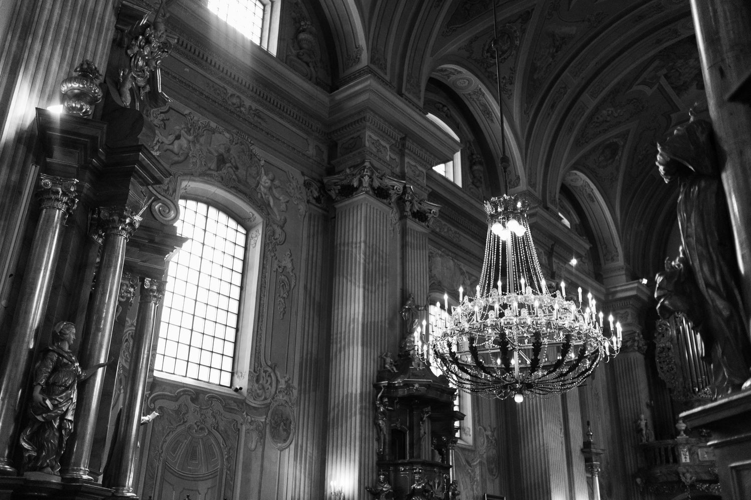 Ornate crystal chandelier hangs in a dramatic baroque church interior with vaulted ceilings and detailed architectural elements.