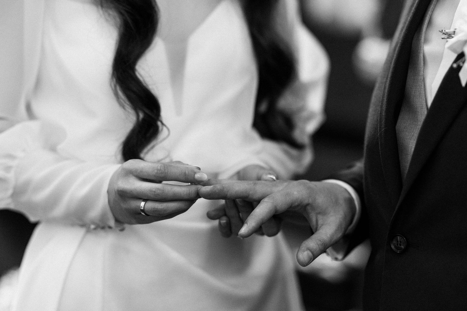 Black and white close-up photo of a wedding ring exchange ceremony between two hands.