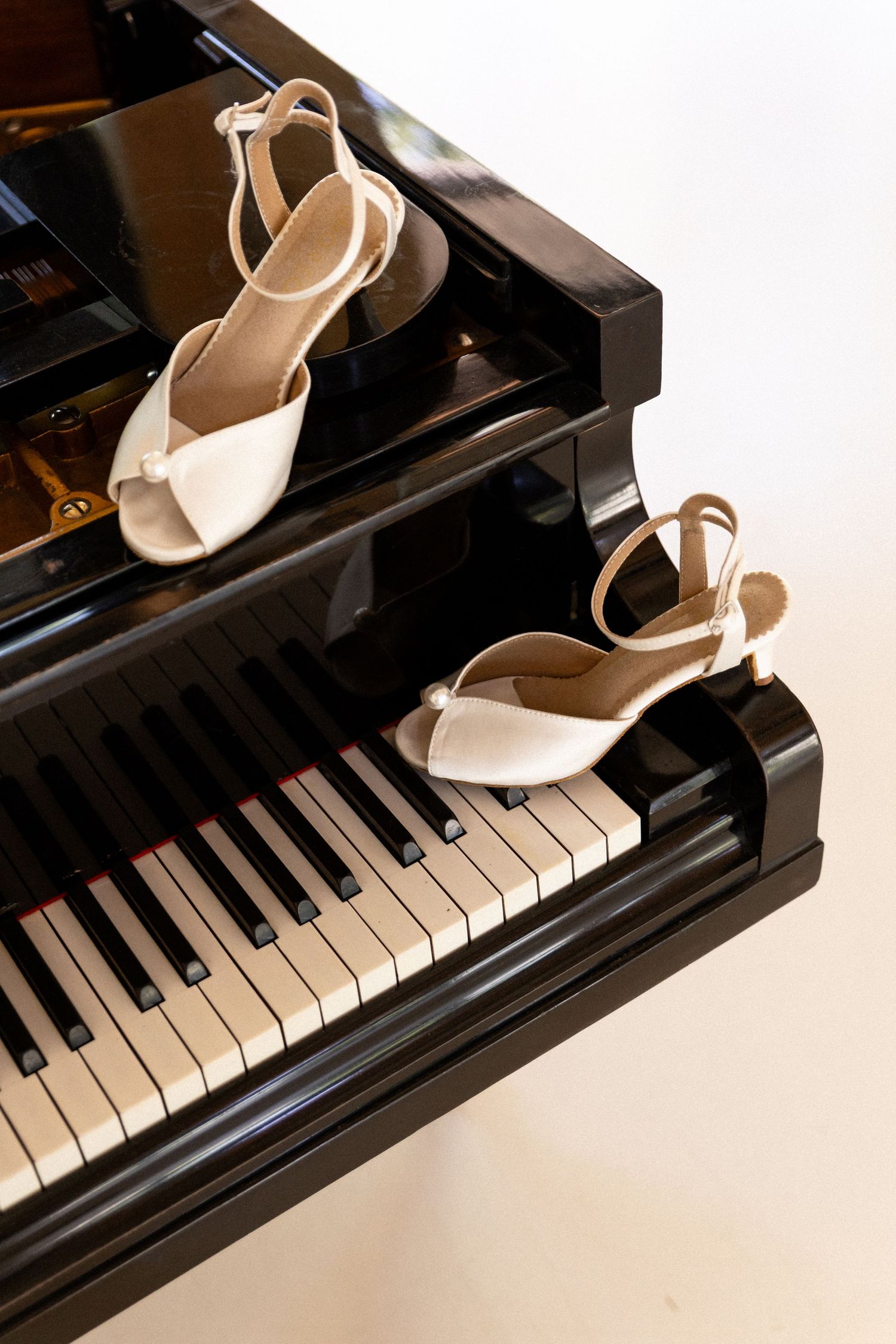 Elegant white bridal sandals placed on black piano keys create a romantic wedding day composition.