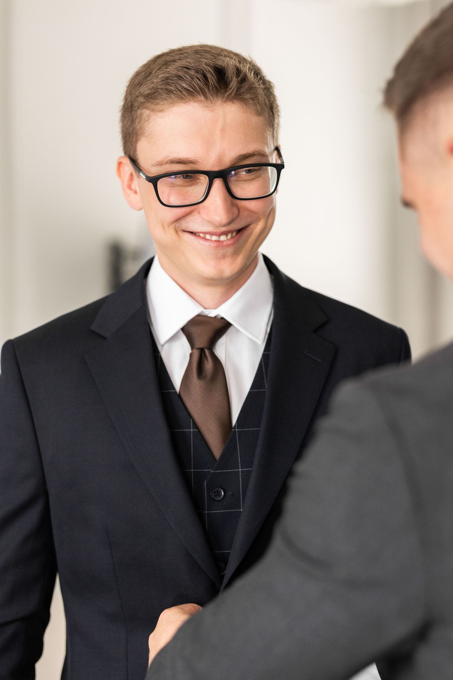 Professional wearing glasses and dark suit smiles during business meeting in bright office setting.
