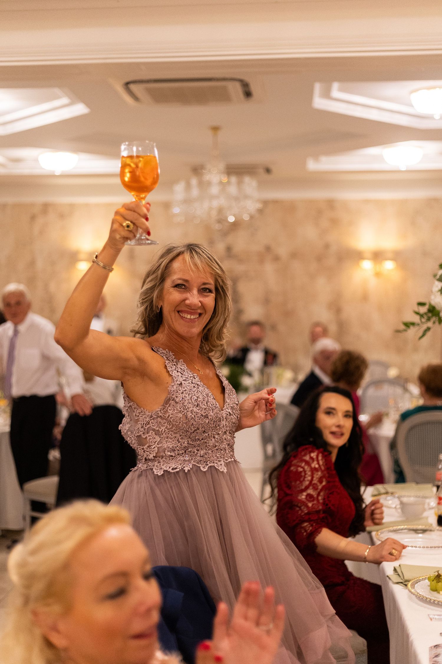 A person in a sparkly gray dress raises their glass in celebration at an elegant wedding reception.