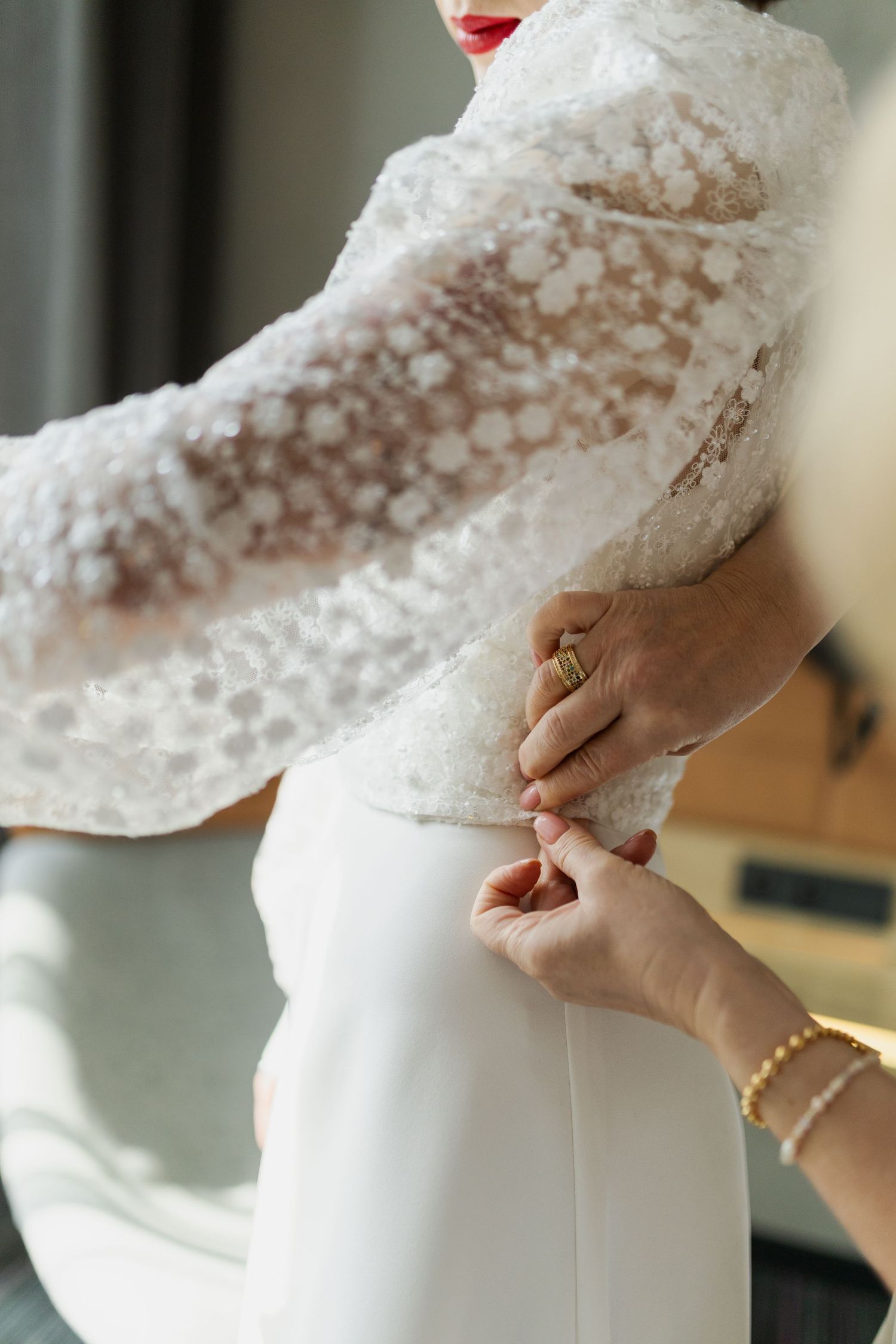 Hands adjusting the delicate lace detail on a white wedding dress during final fitting preparations.