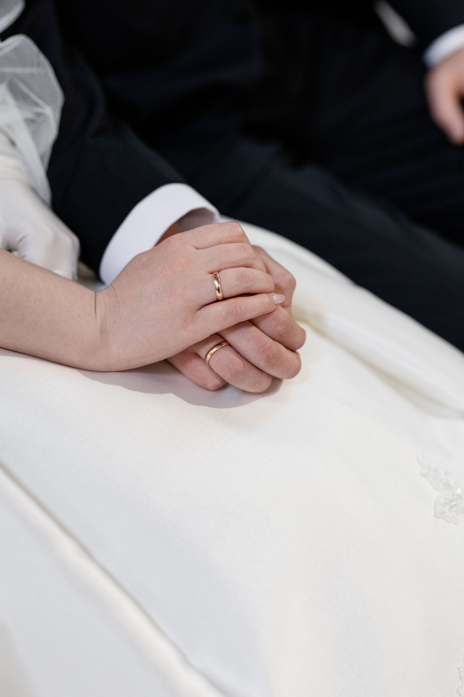 Two hands with wedding rings clasped together on white fabric showing an intimate wedding moment.