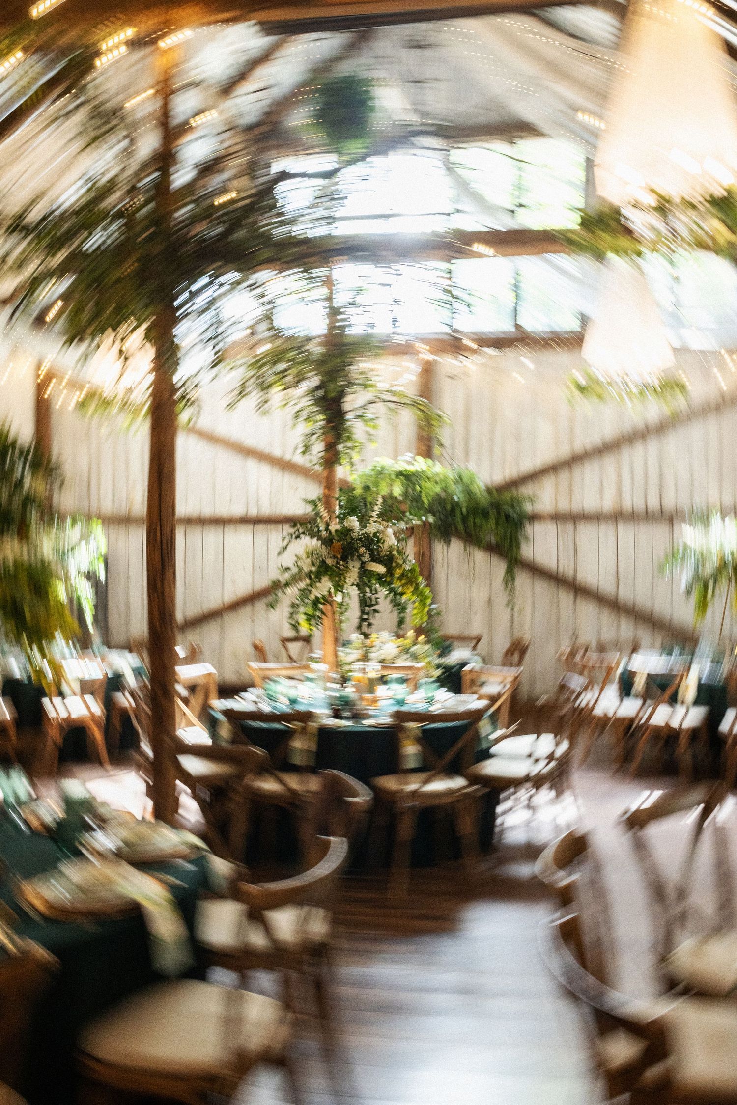 Blurred interior view of a greenhouse dining room with round tables and natural decor under a glass ceiling.