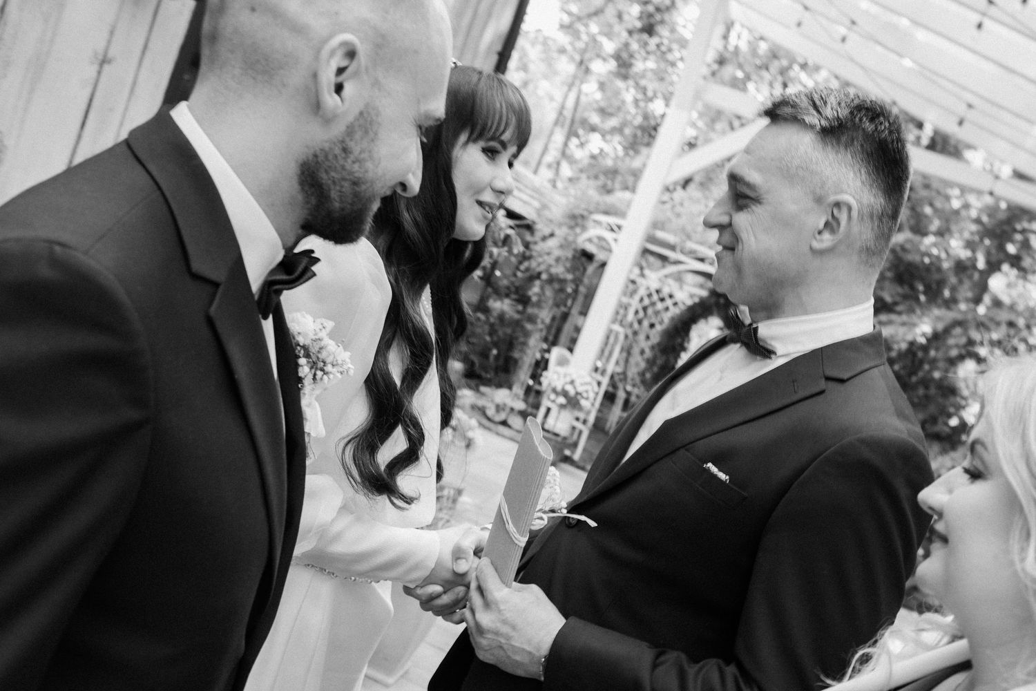 Black and white photo of an emotional wedding ceremony moment between newlyweds and officiant exchanging vows outdoors.