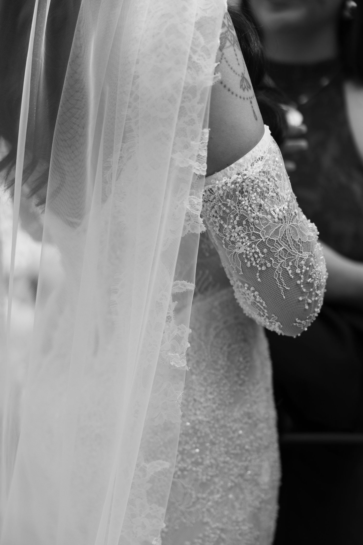 Black and white close-up of a bride in a beaded lace wedding gown with a flowing veil draped elegantly.
