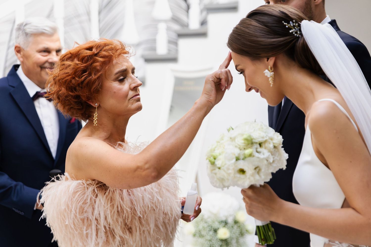 An elegant wedding moment captured with a white bouquet and feathery blush-colored dress details.