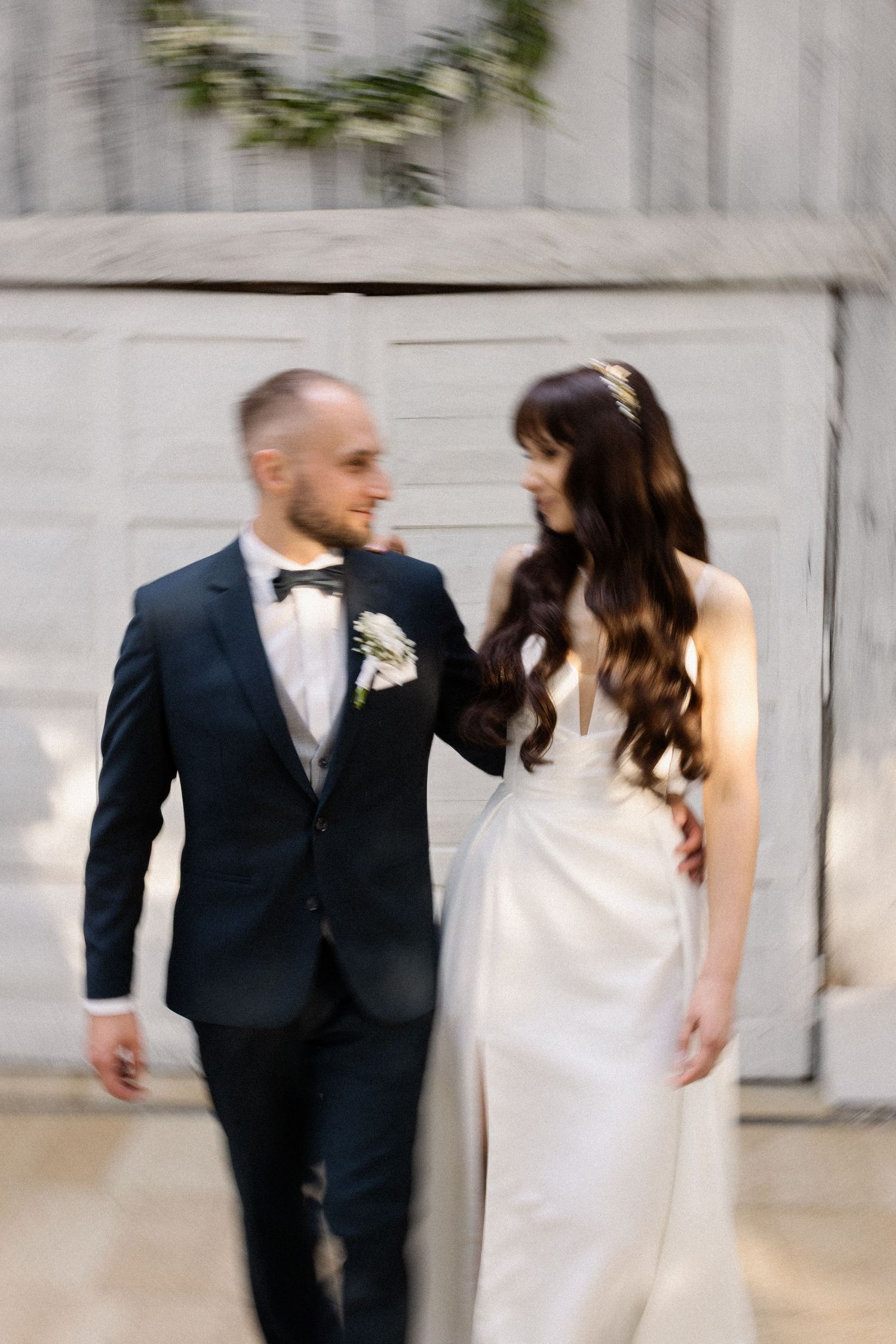 A bride and groom share a joyful moment together while walking, she in white and he in a dark suit with bowtie.