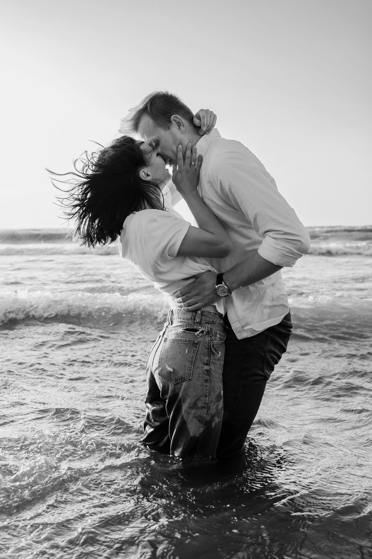 Romantic black and white photo of couple embracing in ocean waves.