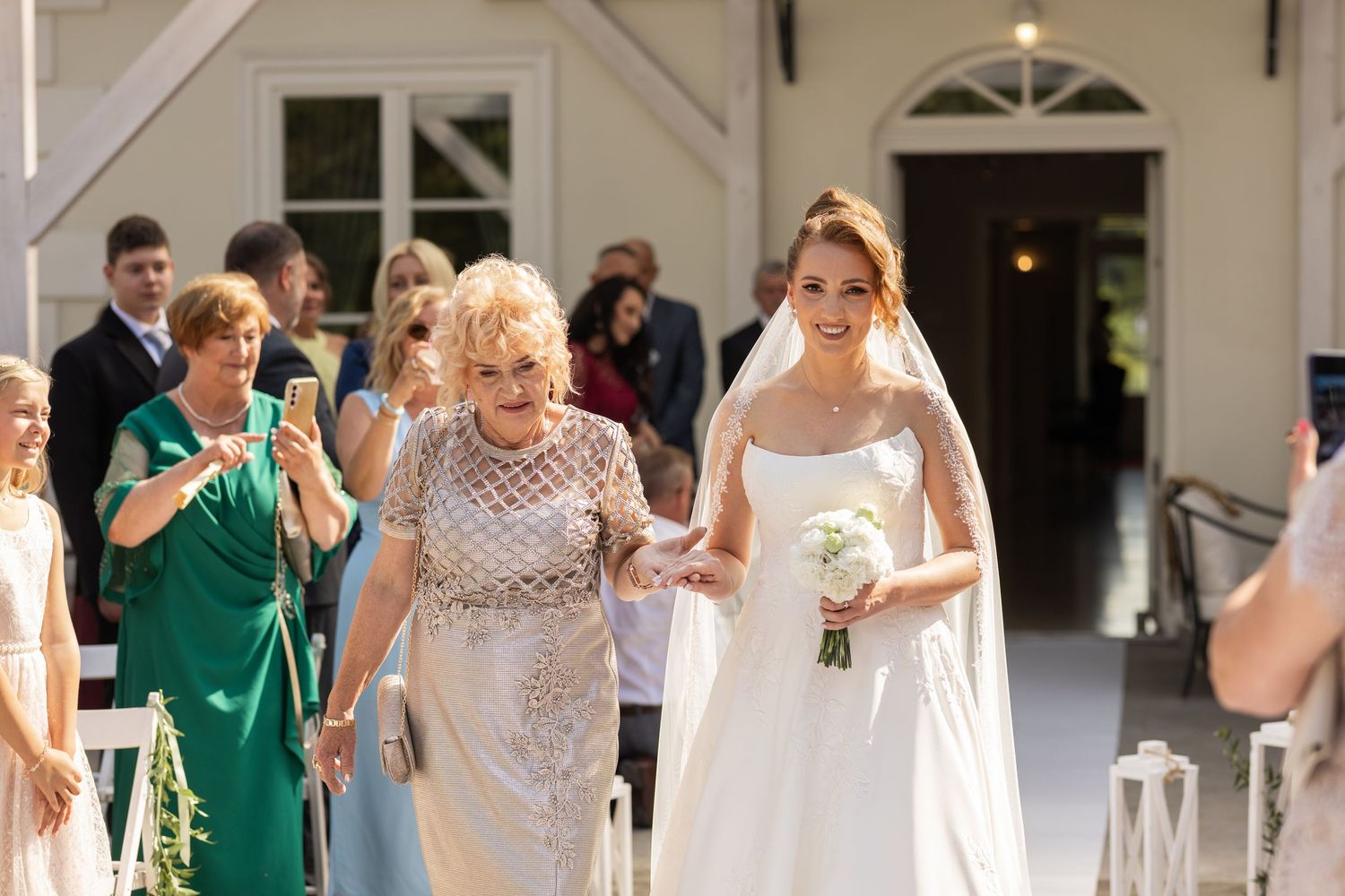 Wedding party guests in green and white attire walk down a covered outdoor corridor during a celebration.