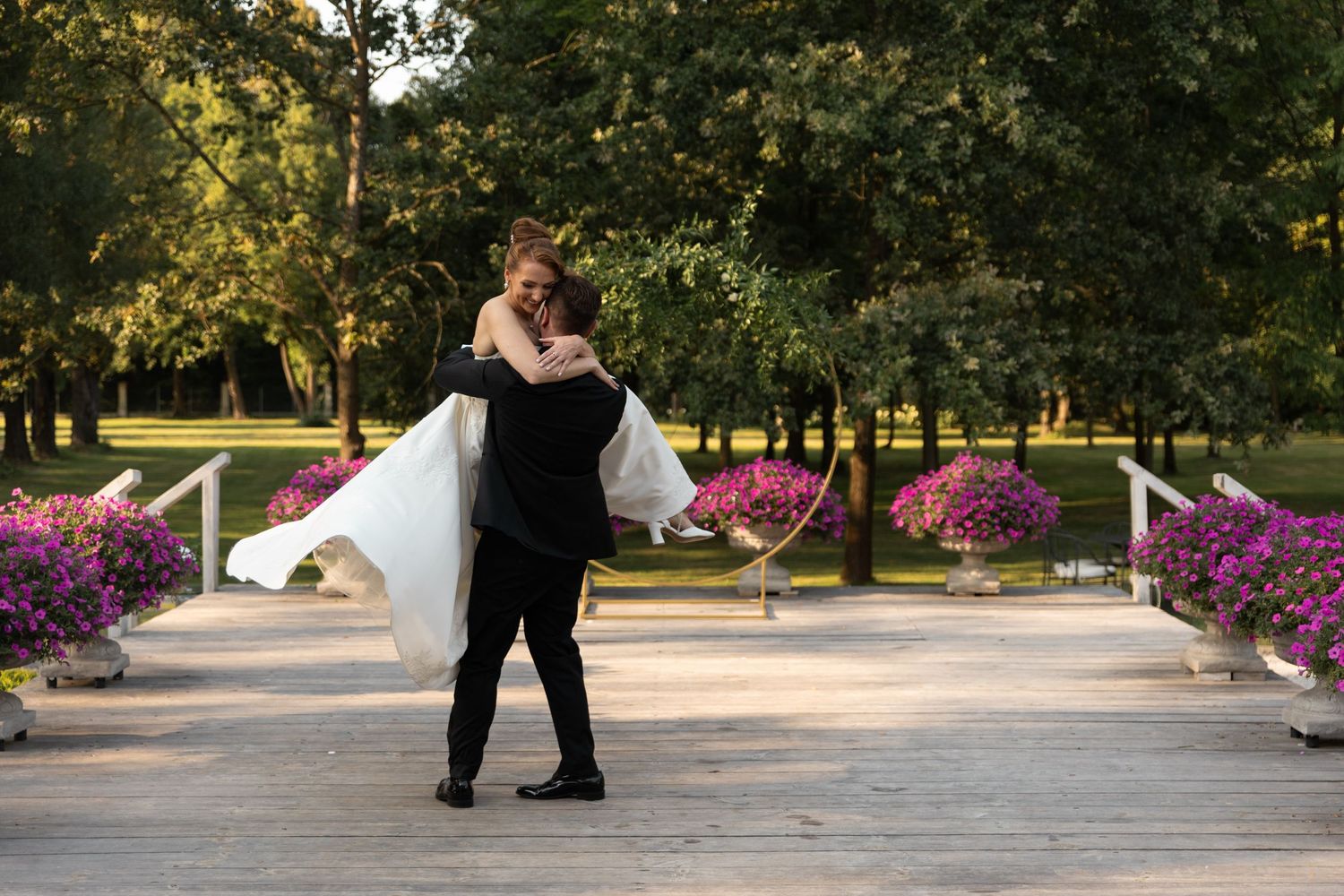 Two dancers perform an elegant tango move on a sunlit path surrounded by blooming purple flowers and trees.