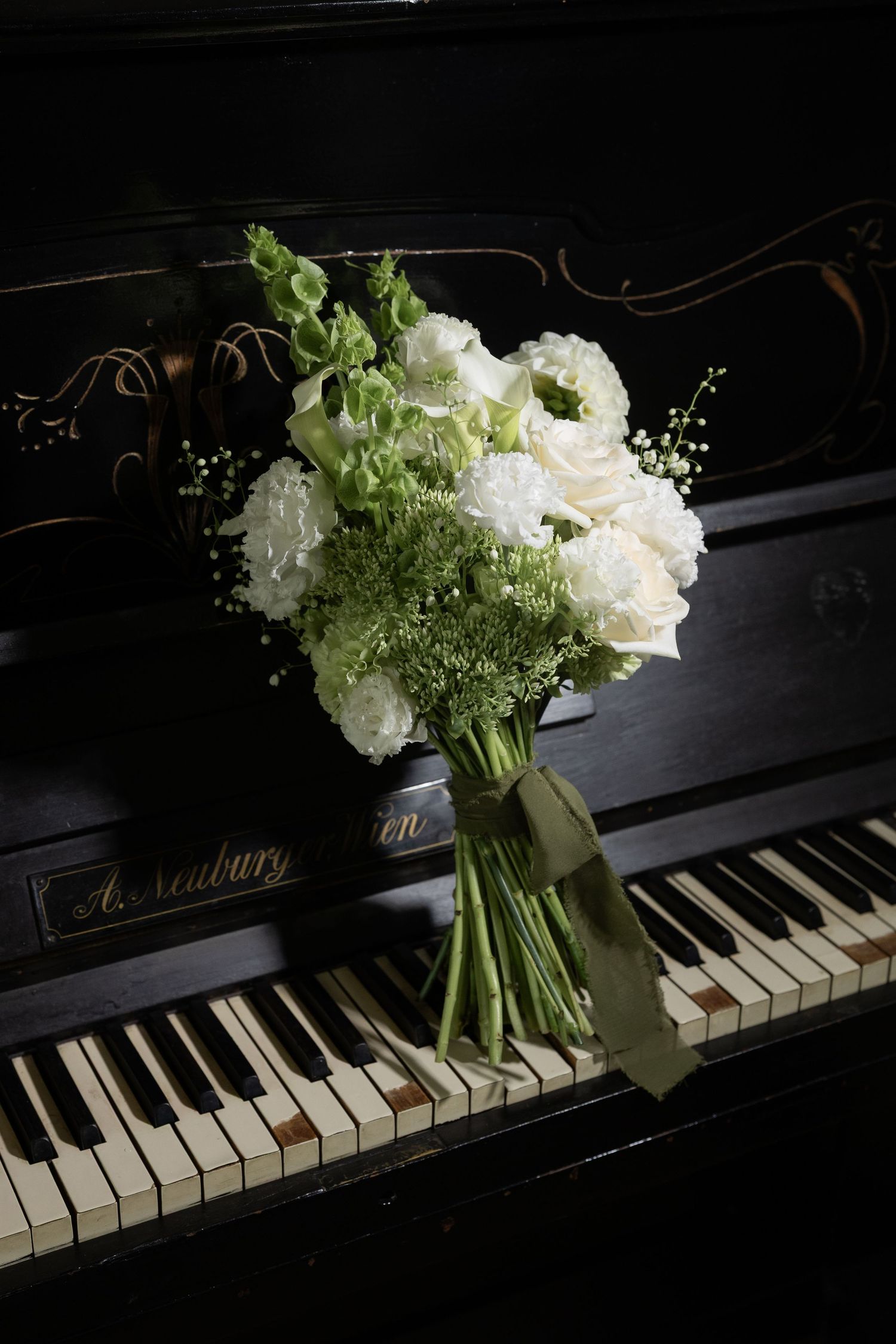 White floral bouquet with roses and greenery resting on vintage black upright piano keys.